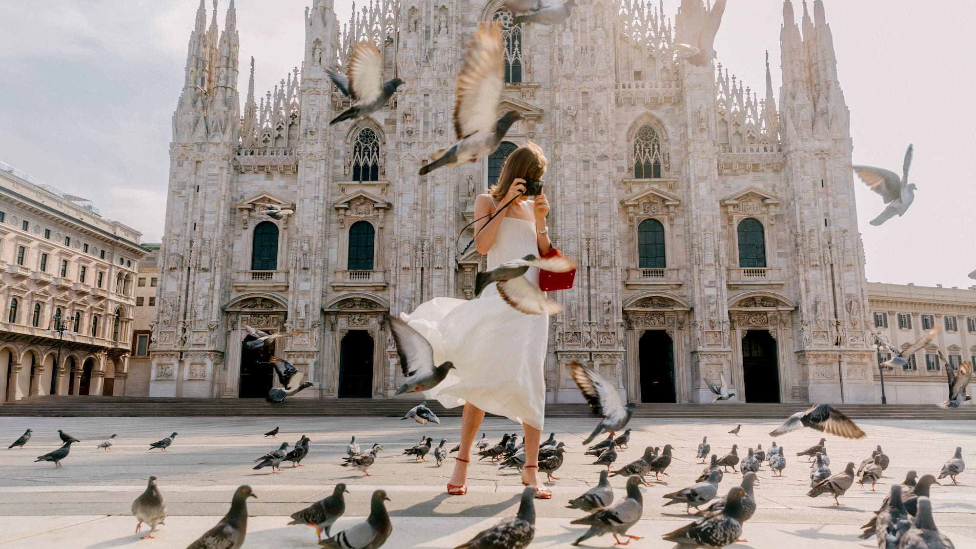 a woman in a white dress taking a picture of pigeons in front of a building