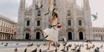 a woman in a white dress taking a picture of pigeons in front of a building