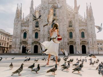 Traveler photographing Milan Duomo. Pigeons fly around Italian Gothic cathedral.