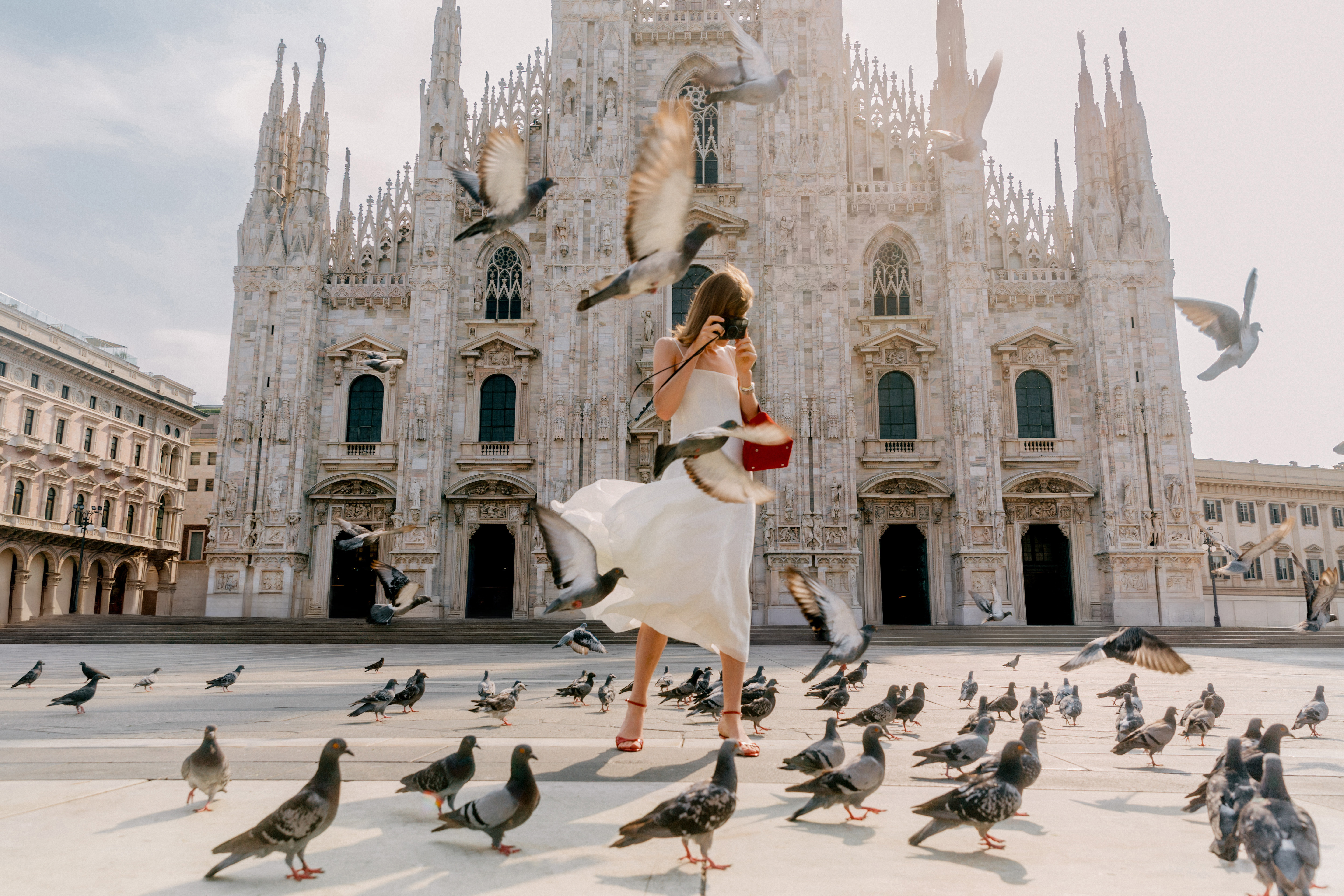 a woman in a white dress taking a picture of pigeons in front of a building