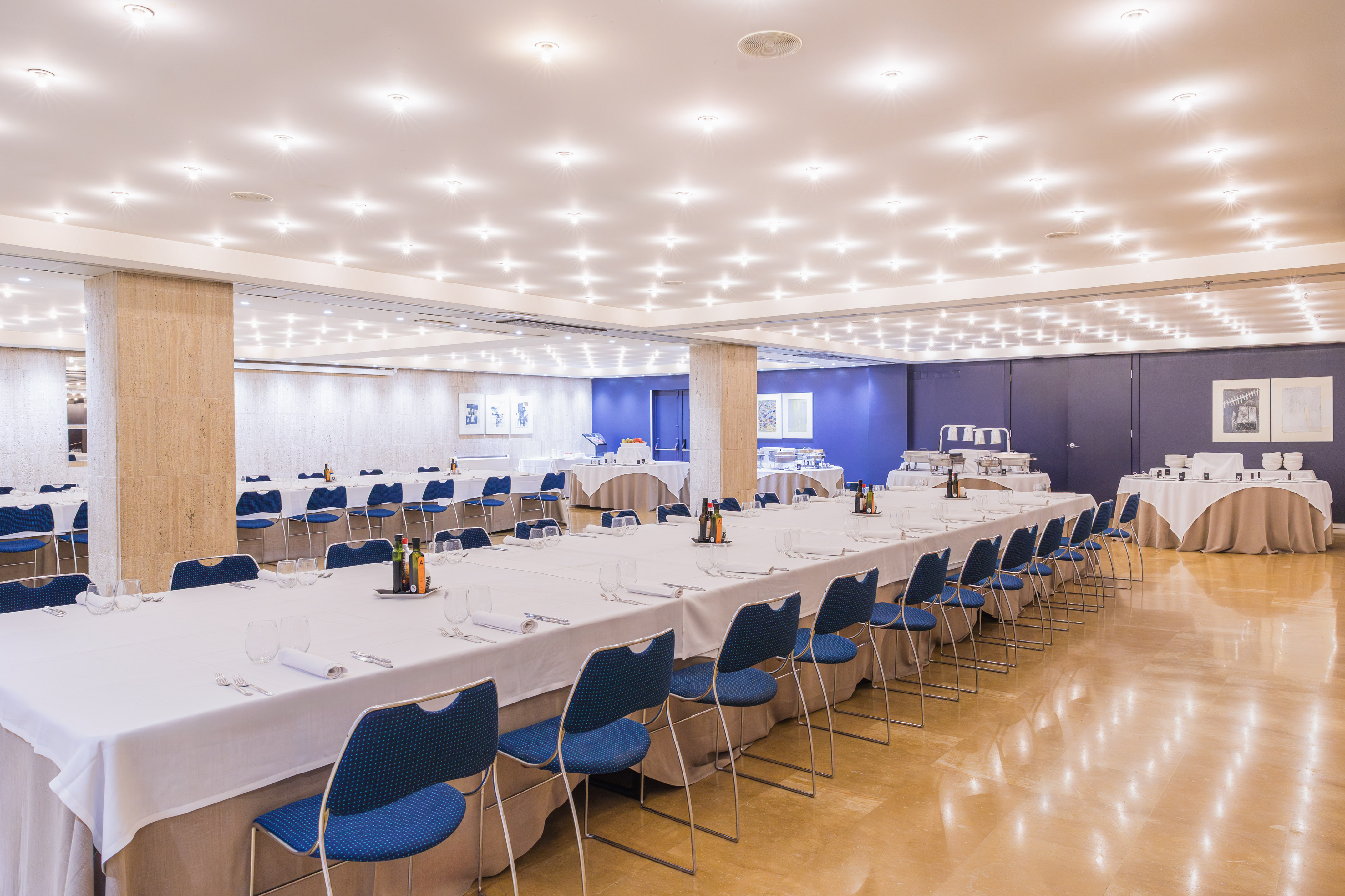 Spacious banquet hall set with long tables, blue chairs, and buffet stations.