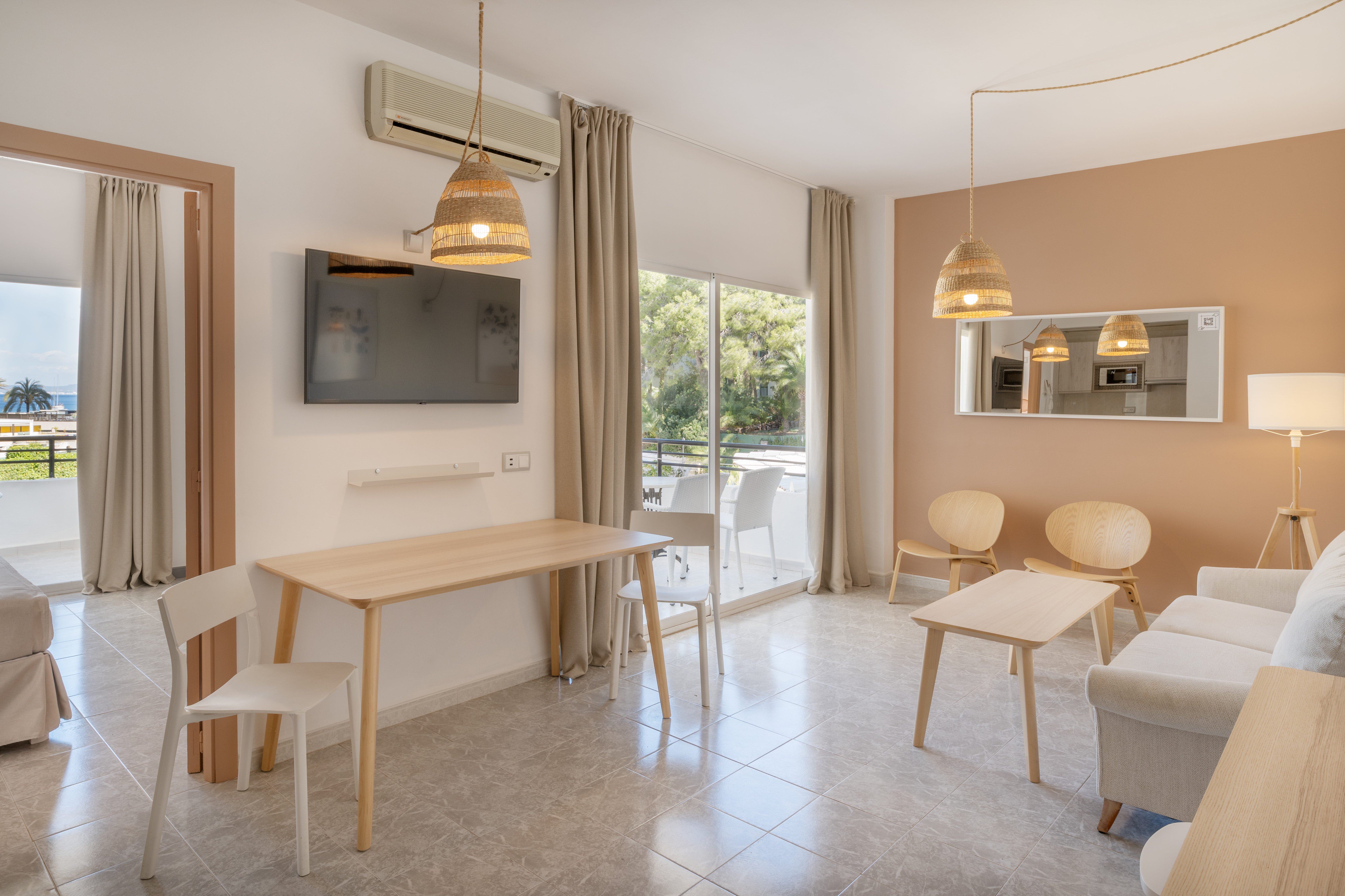 Modern studio apartment with neutral decor, TV, wood furniture, and balcony view.