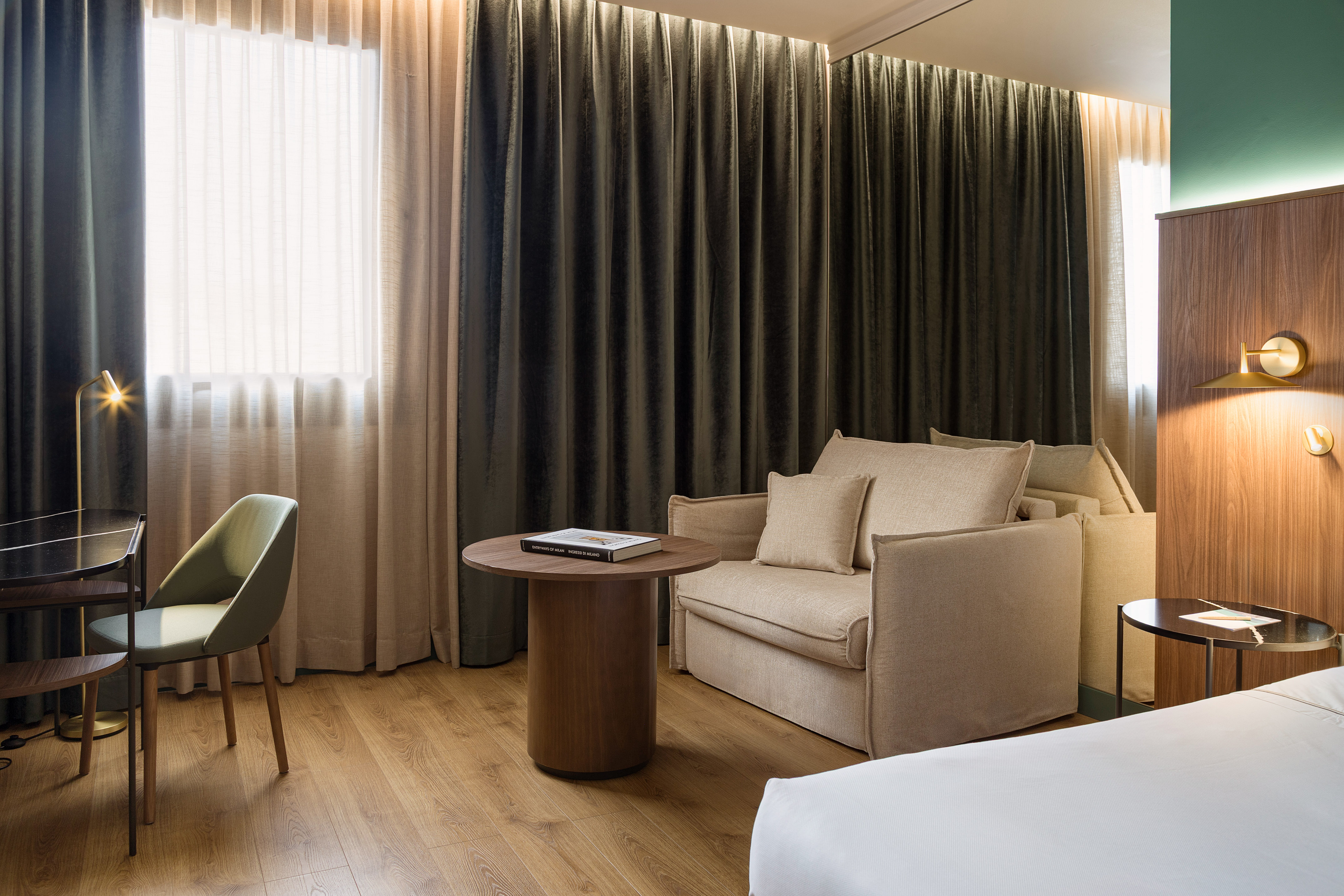 Spacious modern hotel room featuring a sofa, desk, green chair, and dark curtains.