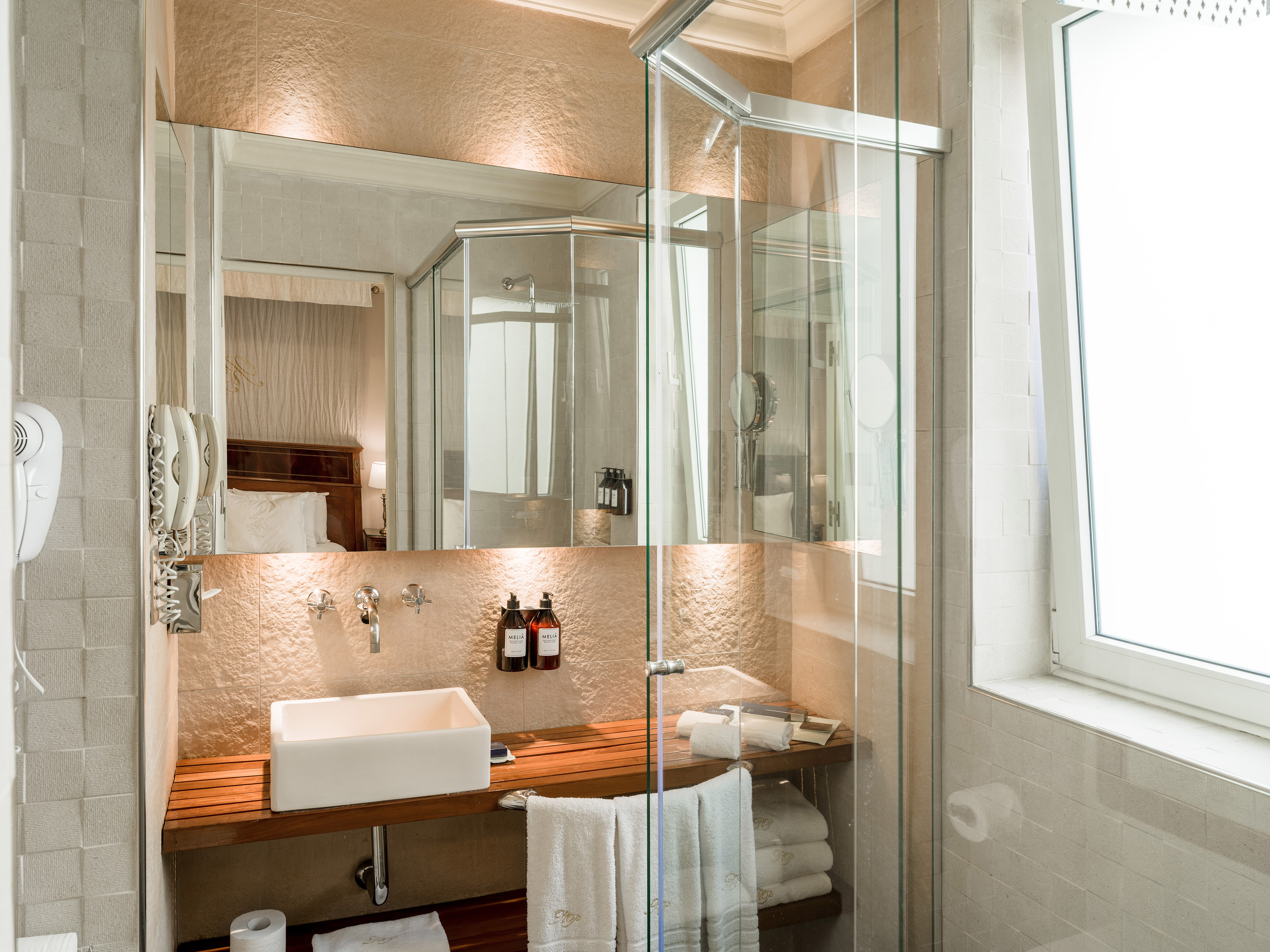 Modern hotel bathroom: white sink, wooden counter, large mirror, glass shower.