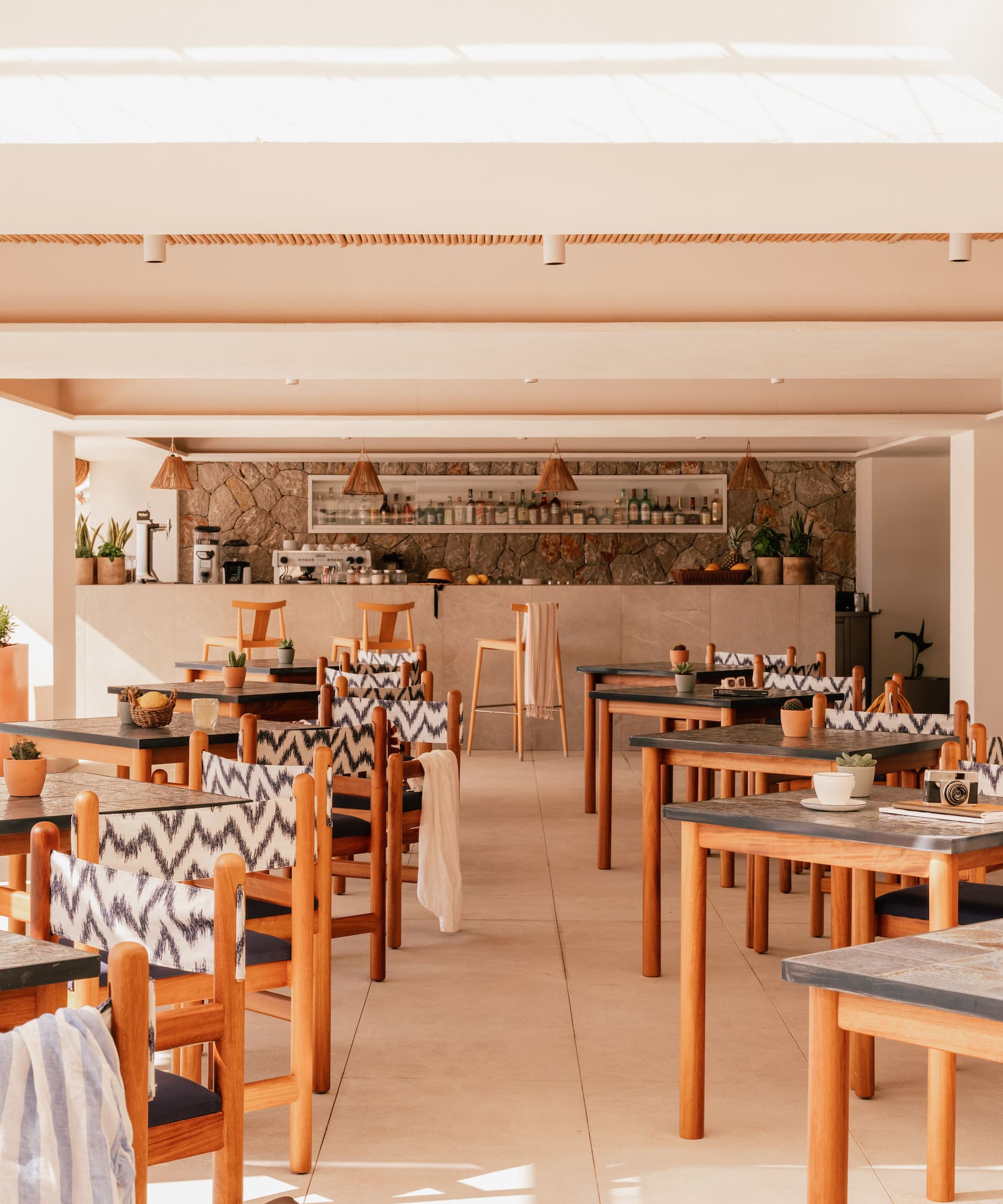 Bright resort restaurant with wooden tables, patterned chairs, and bar.