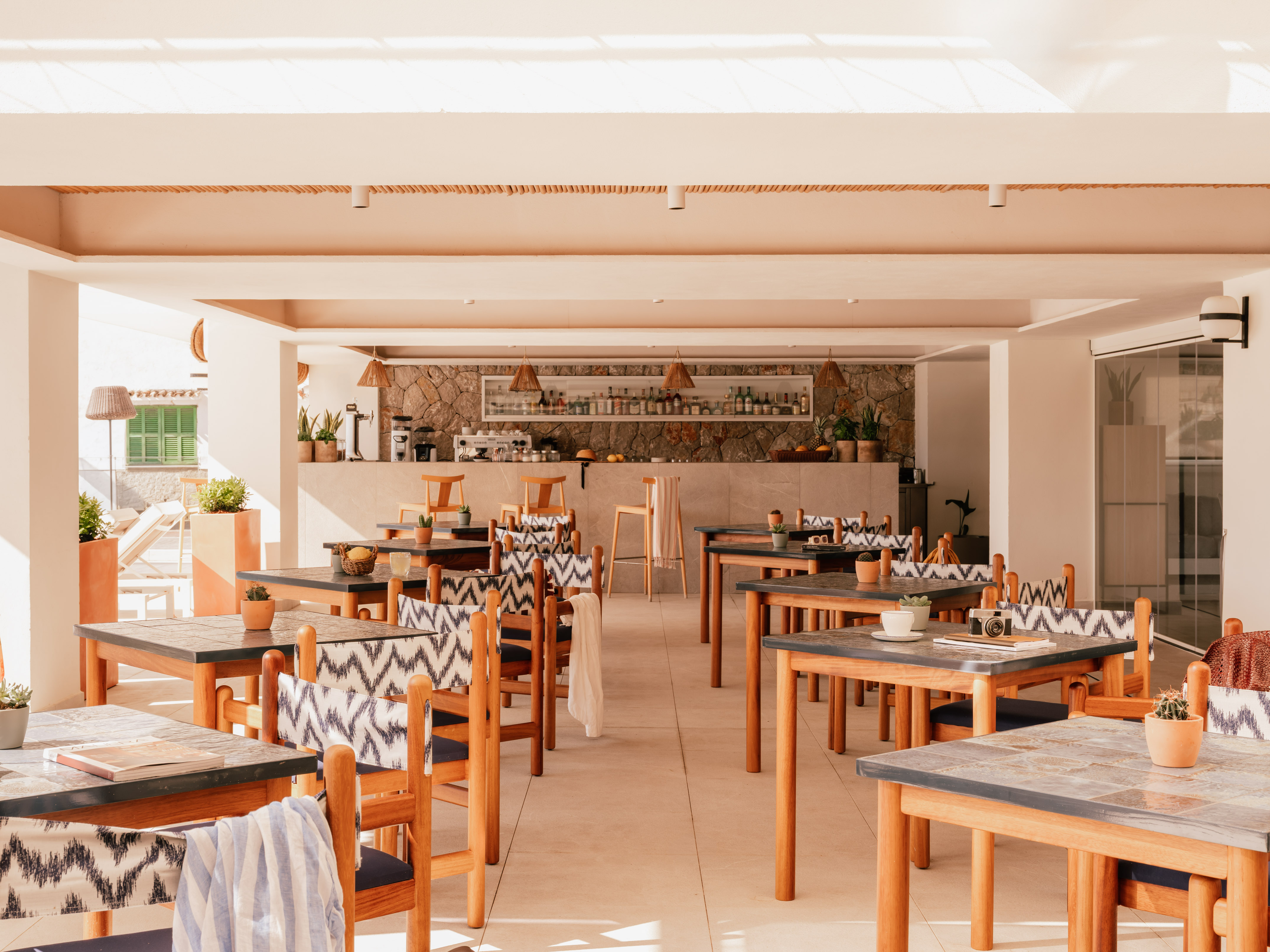 Bright resort restaurant with wooden tables, patterned chairs, and bar.