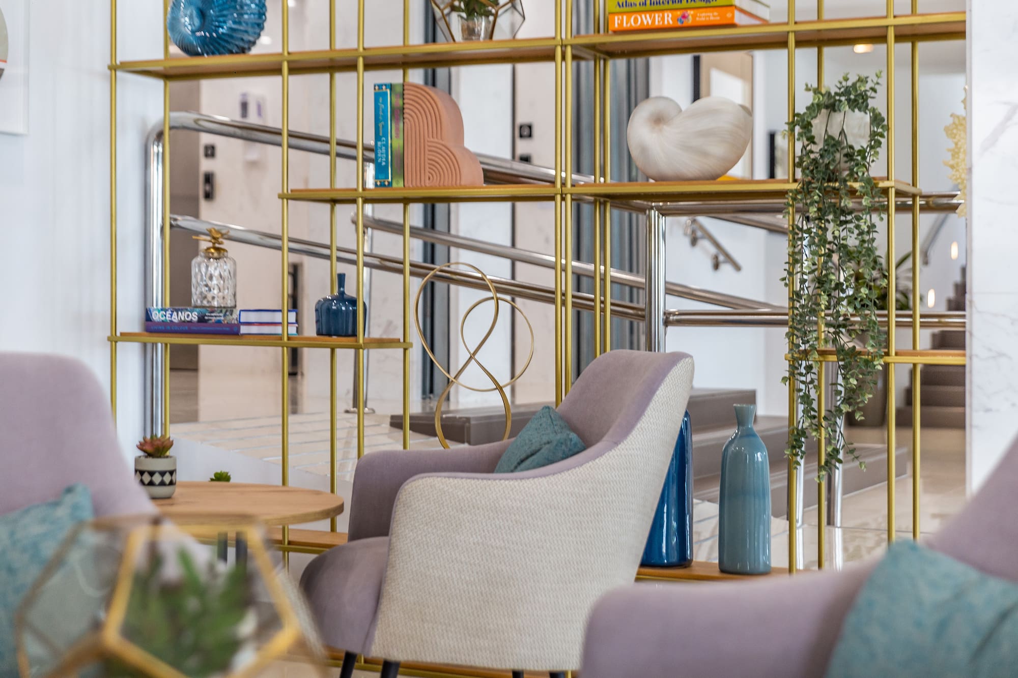 Contemporary lounge with gold shelving, blue vases, books, and armchairs.