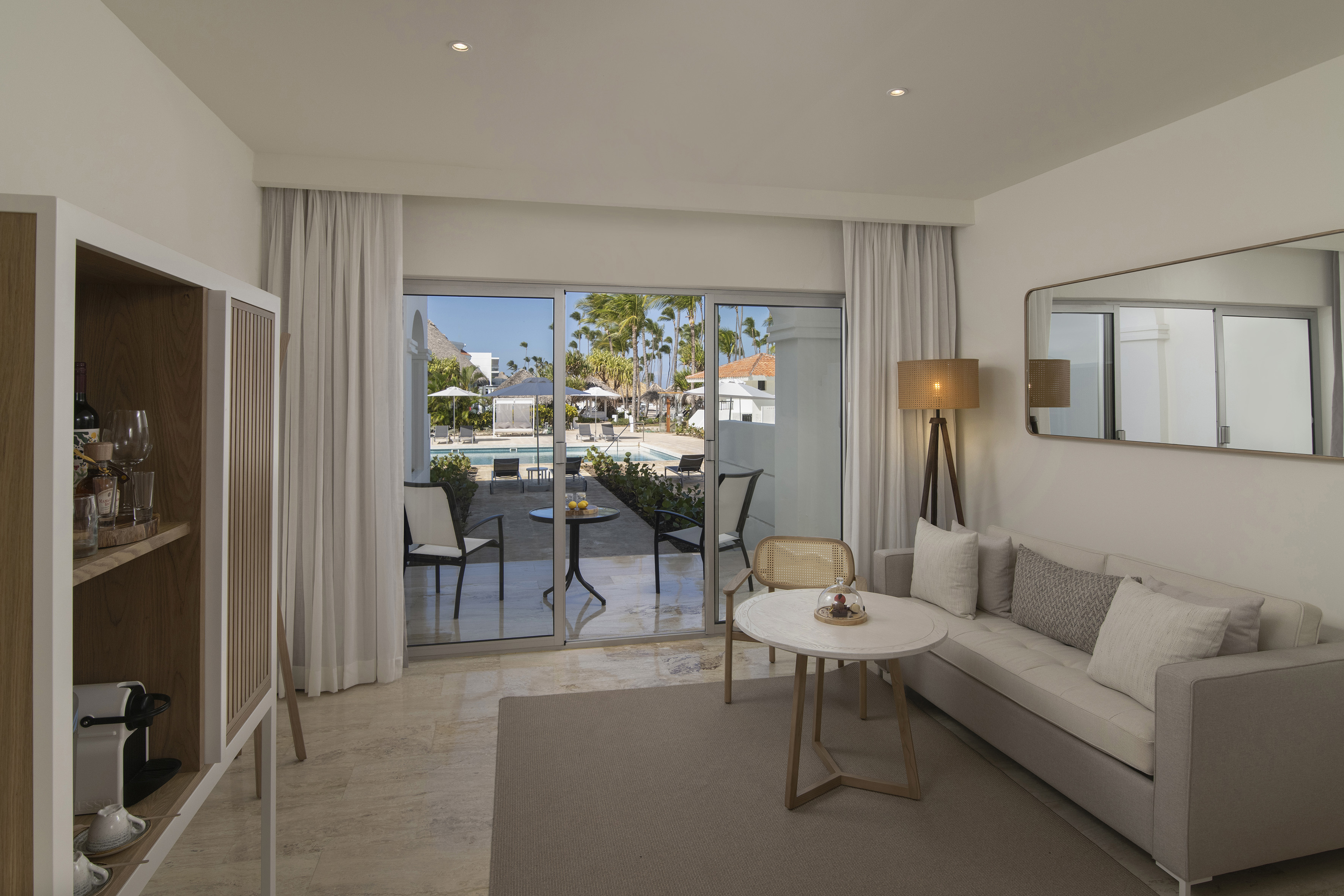 Luxury resort suite living area overlooking a swimming pool and palm trees.
