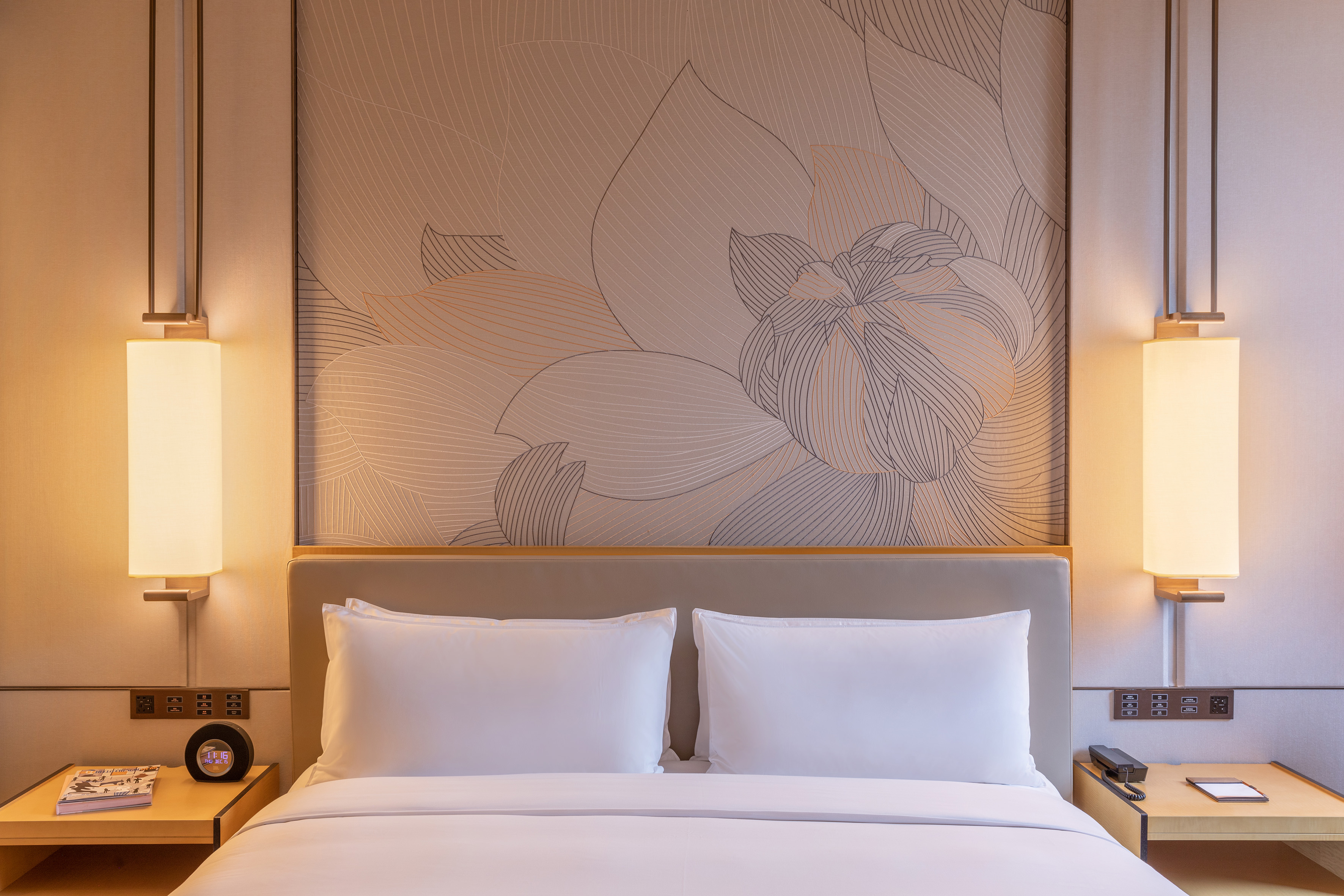 Modern hotel bedroom with king bed, abstract floral wall art, and warm bedside sconces.