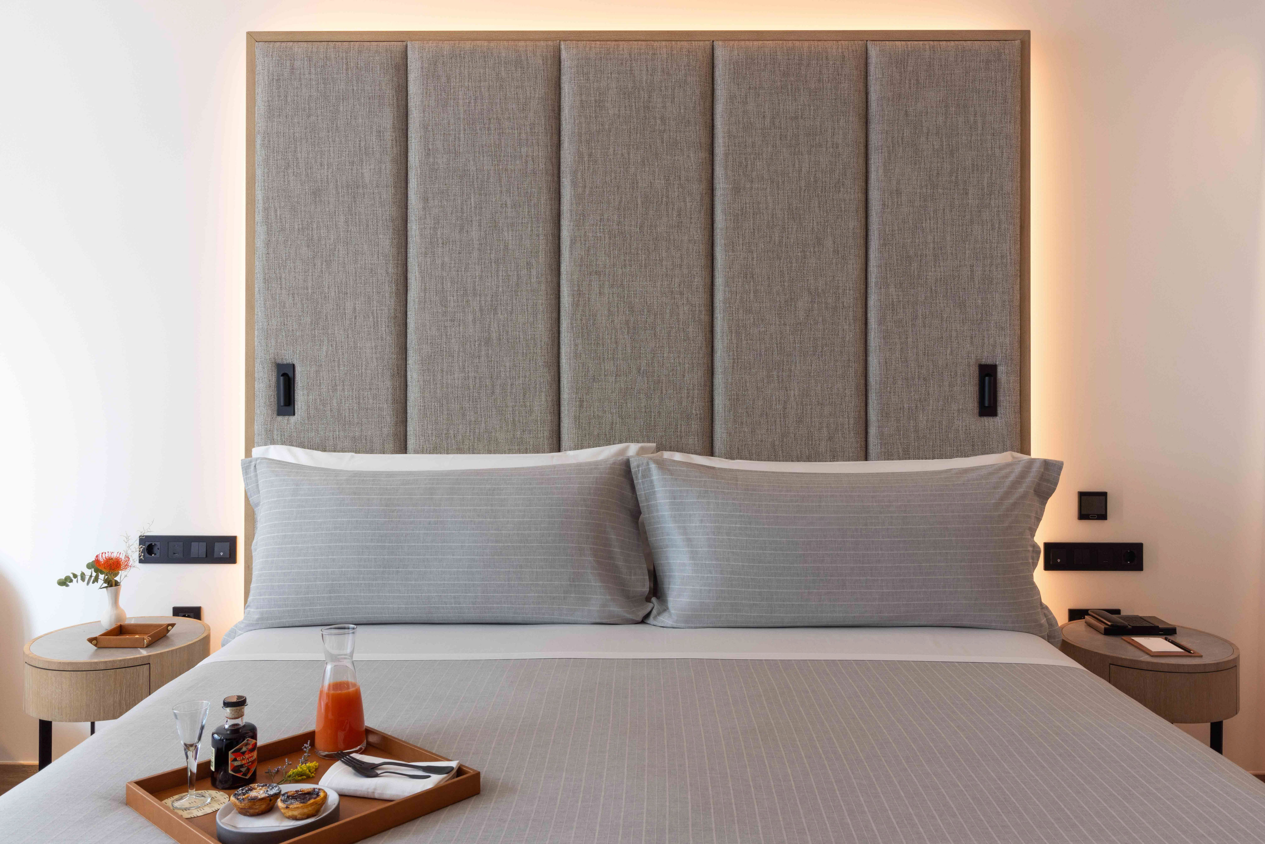 Breakfast in bed on a modern hotel bed with gray bedding and upholstered headboard.