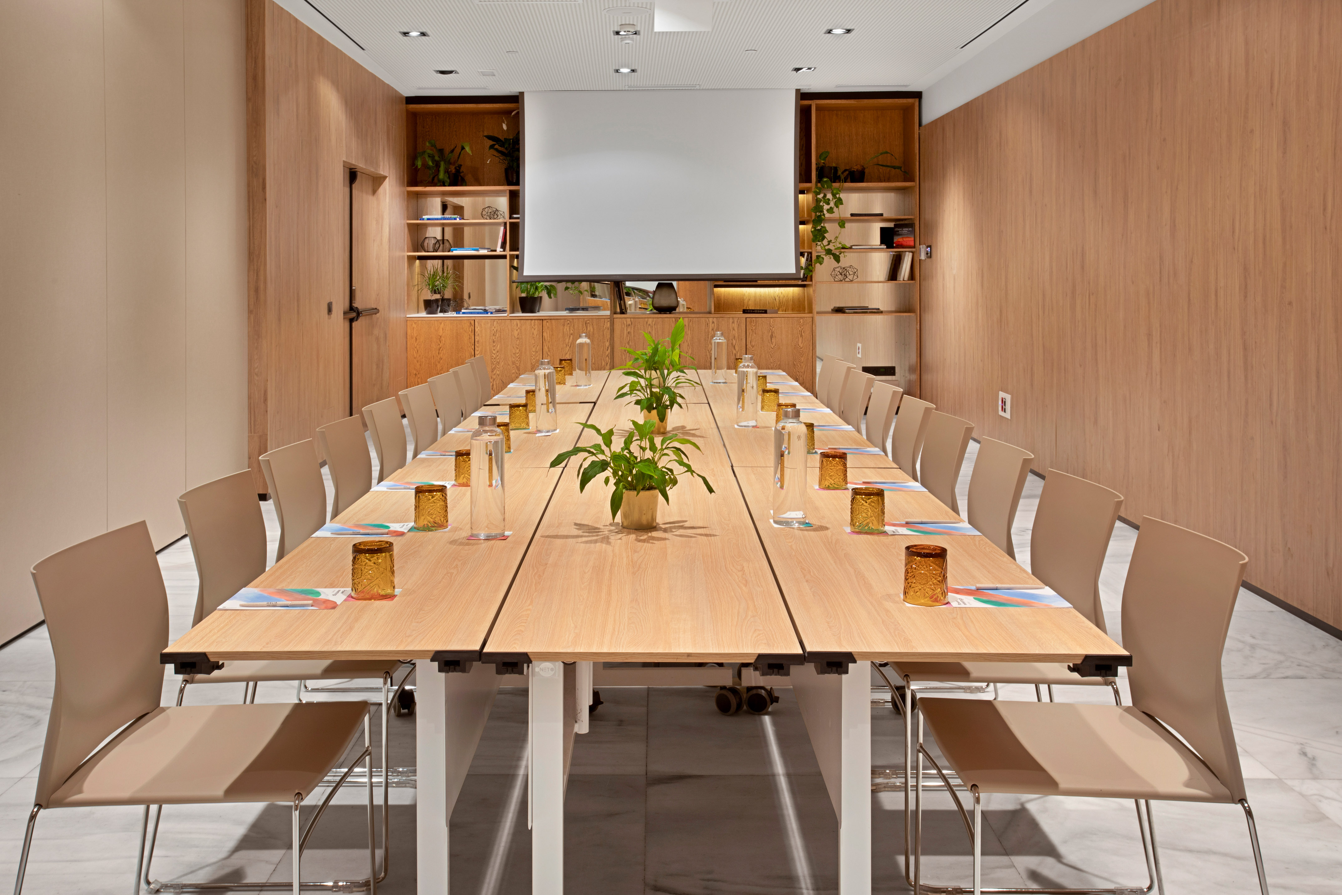 Modern conference room with wooden table, beige chairs, and projector screen.