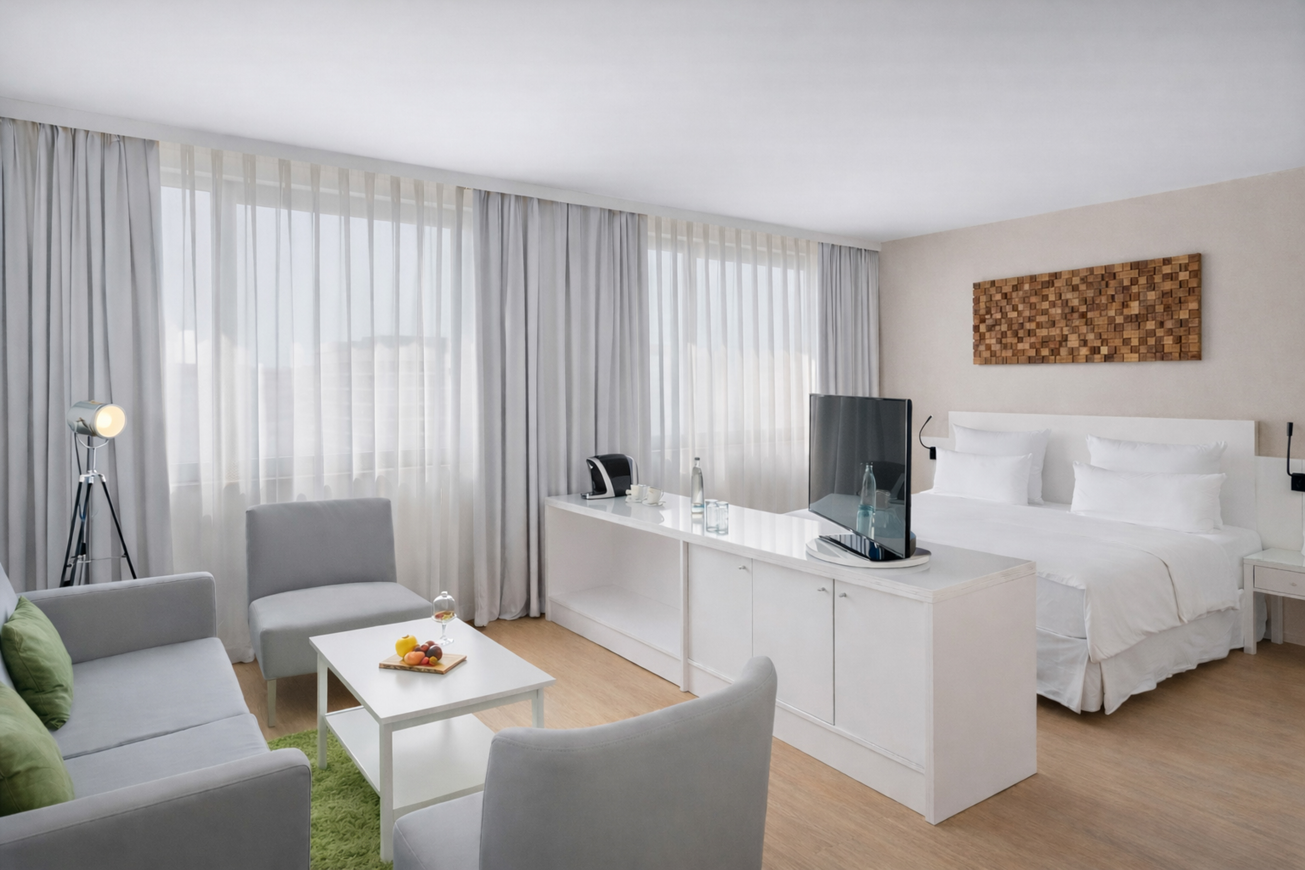 Modern hotel suite with bed, living area, TV, and large windows.