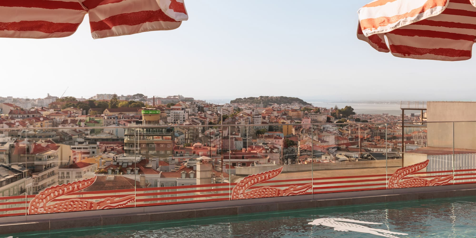 Lacoste rooftop pool with Lisbon skyline, crocodile floats, striped umbrellas.