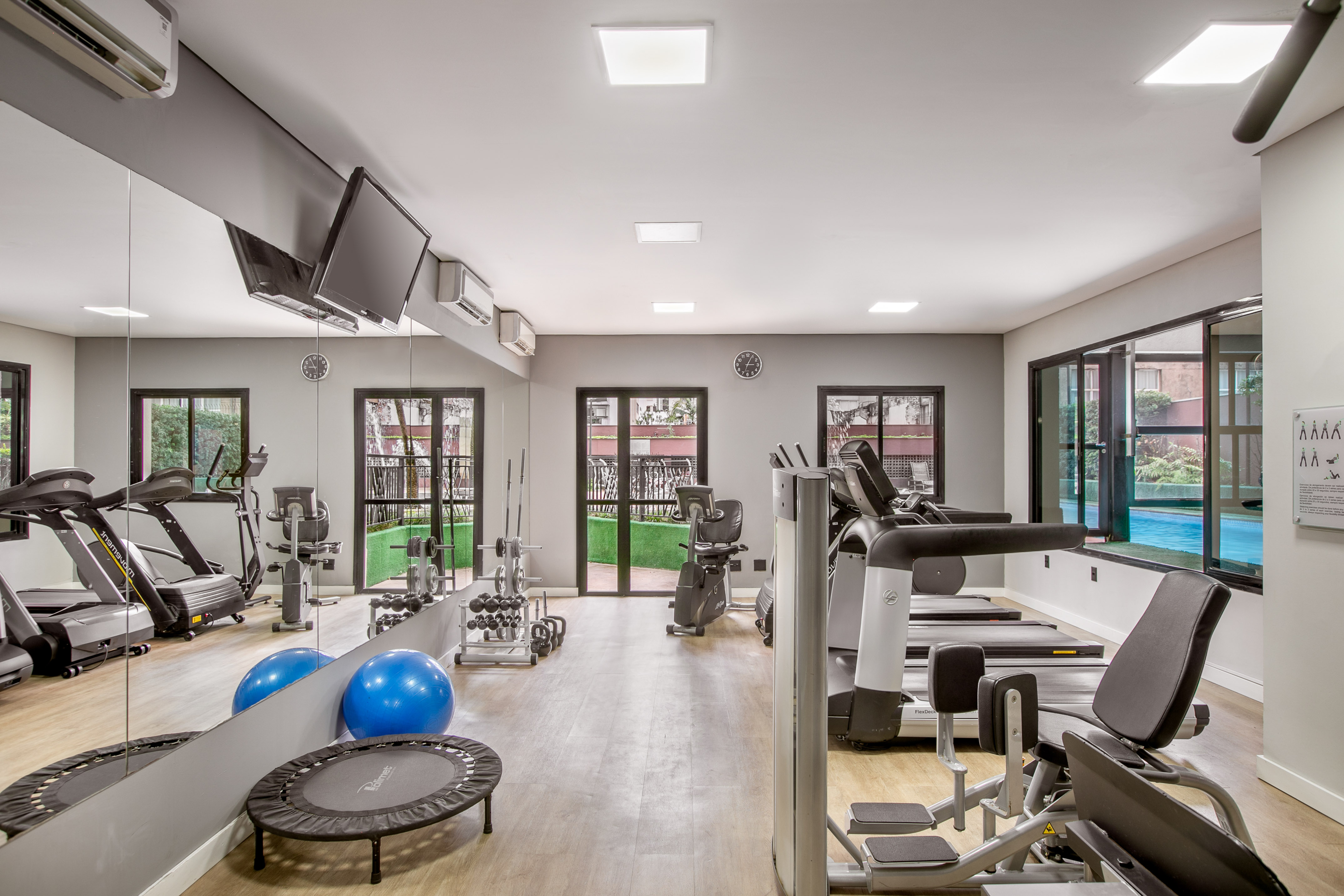 Modern gym interior with exercise equipment, mirrored walls, and pool view.