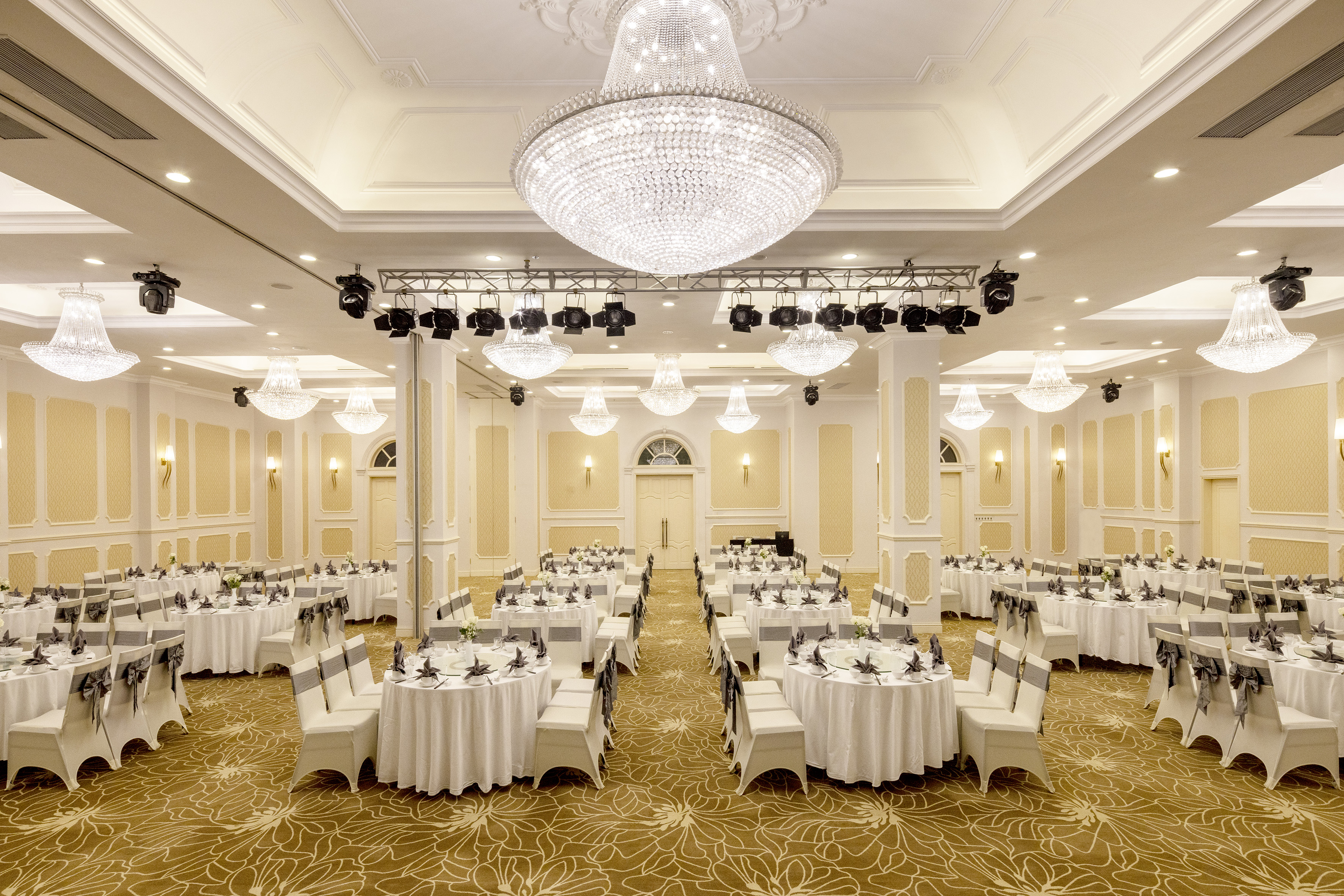 Elegant ballroom with round tables, crystal chandeliers, and event lighting.