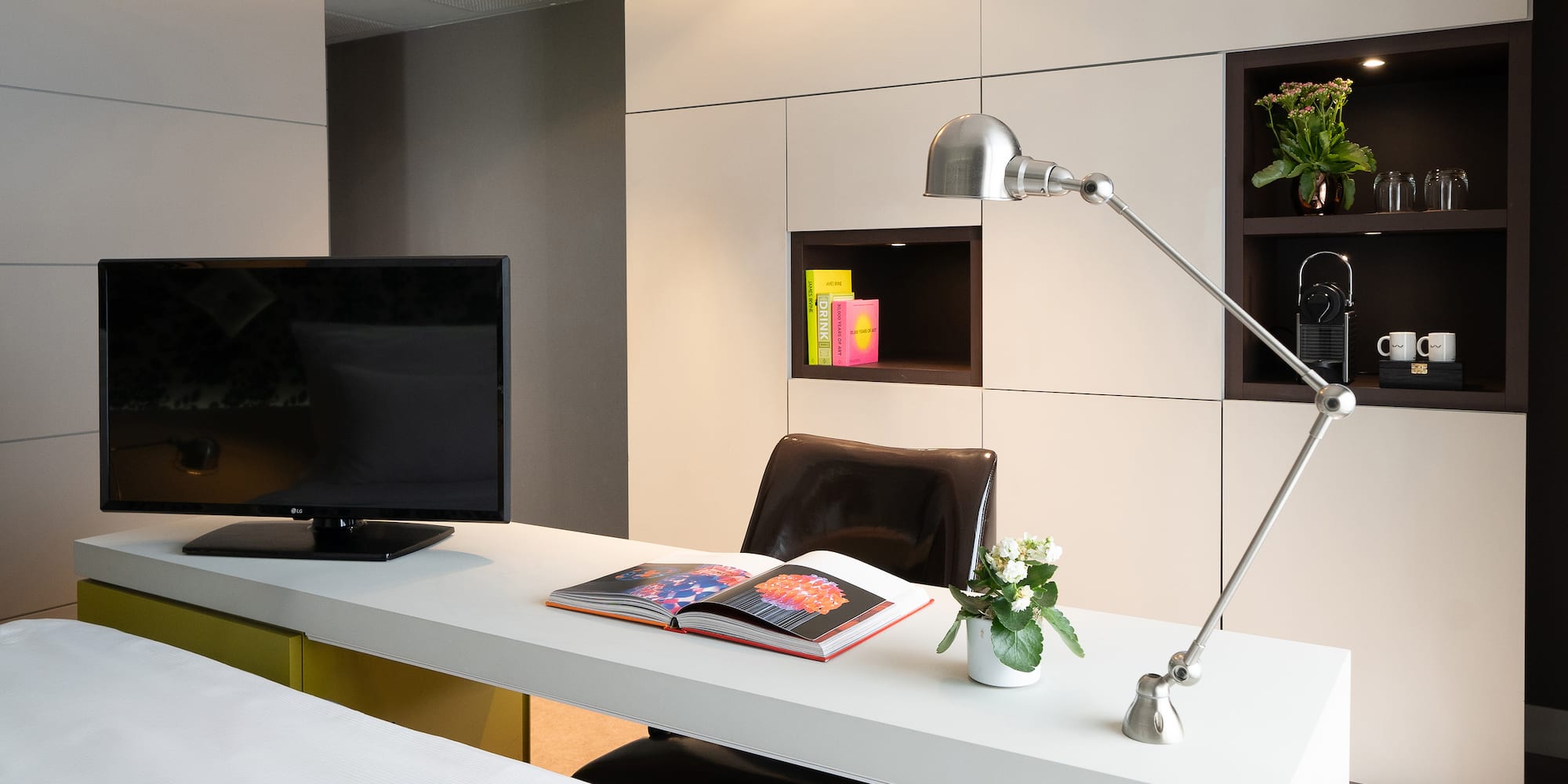 Hotel room workstation with TV, adjustable lamp, open book, and built-in storage.