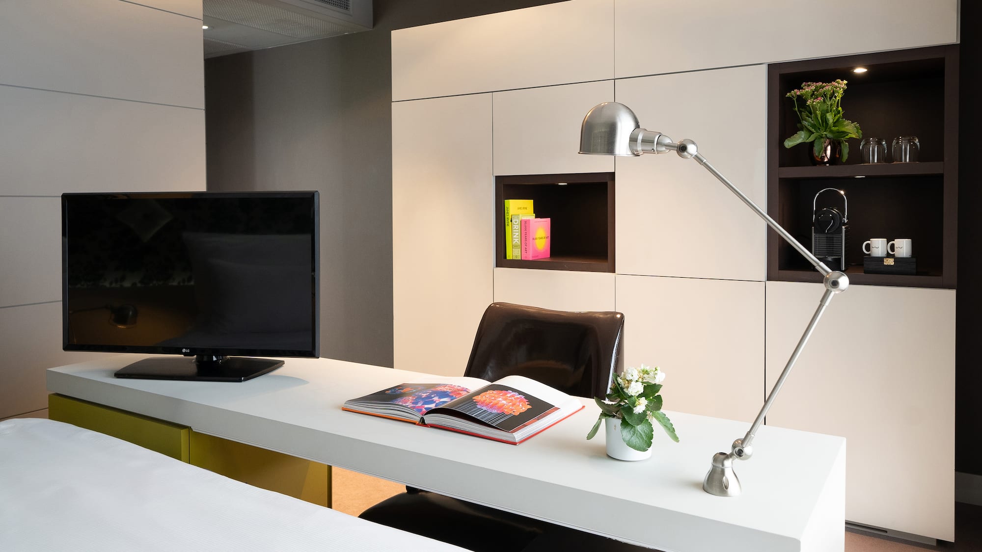 Hotel room workstation with TV, adjustable lamp, open book, and built-in storage.