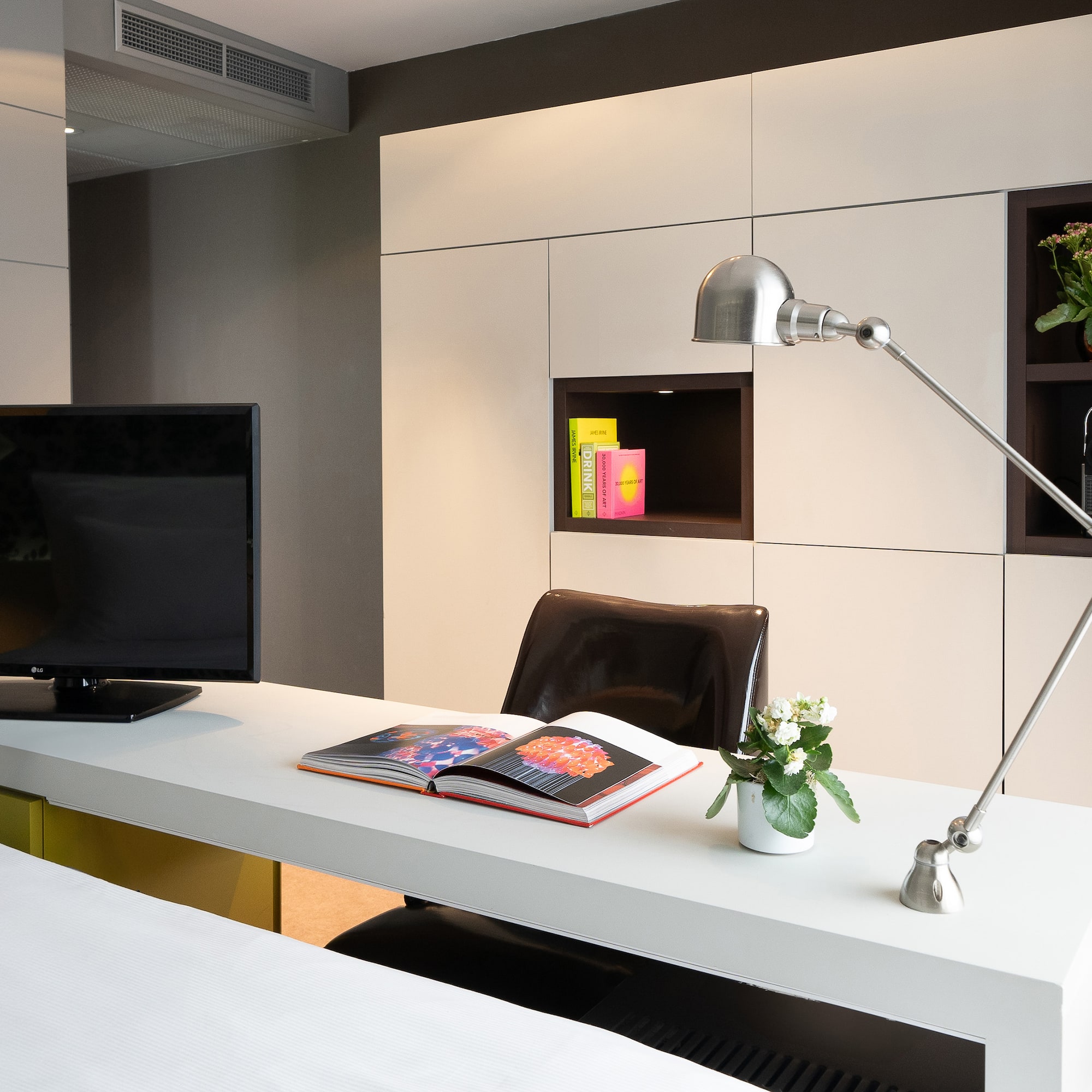 Hotel room workstation with TV, adjustable lamp, open book, and built-in storage.