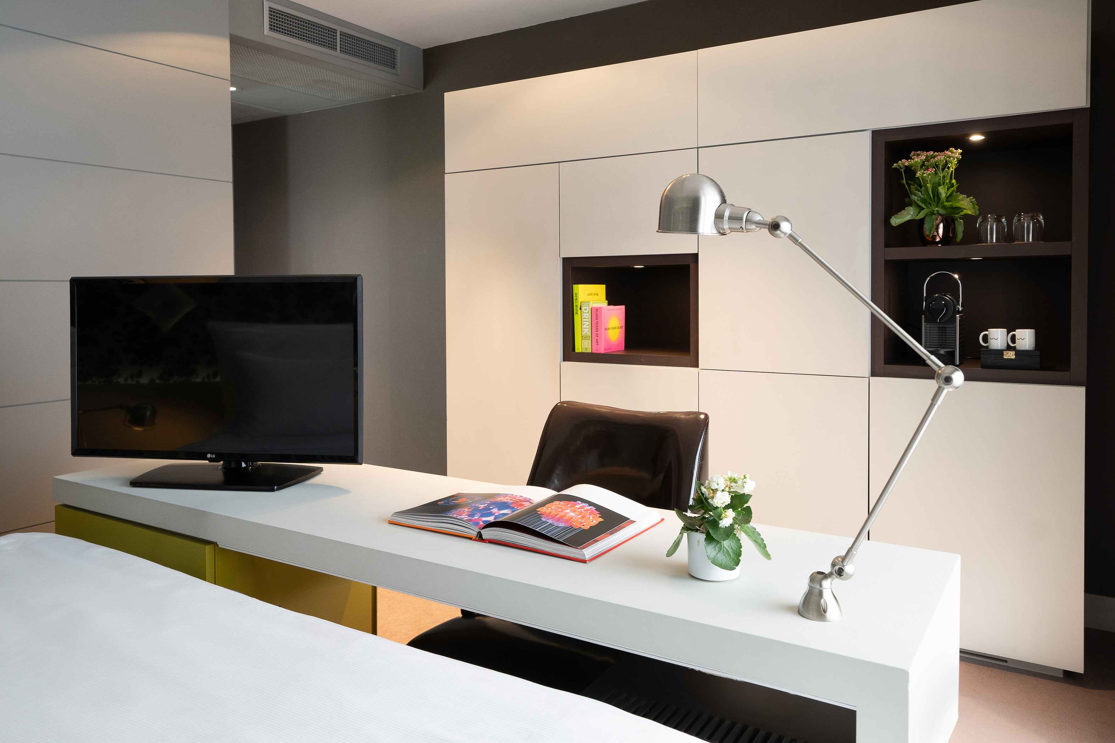 Hotel room workstation with TV, adjustable lamp, open book, and built-in storage.
