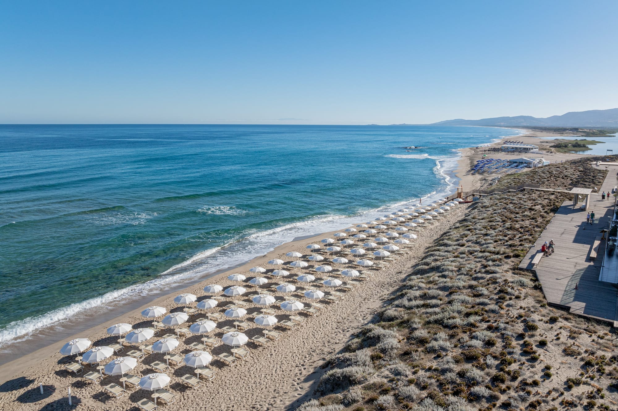 Beach resort with white umbrellas, blue ocean, sandy dunes, and boardwalk.