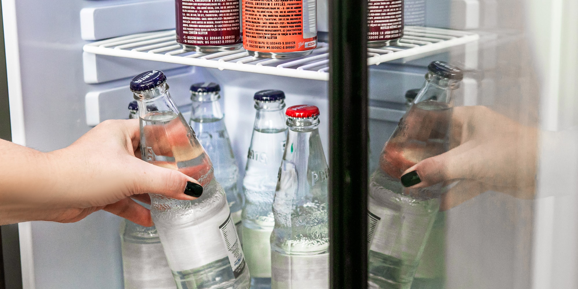 Hand removing a glass water bottle from a stocked mini-fridge.