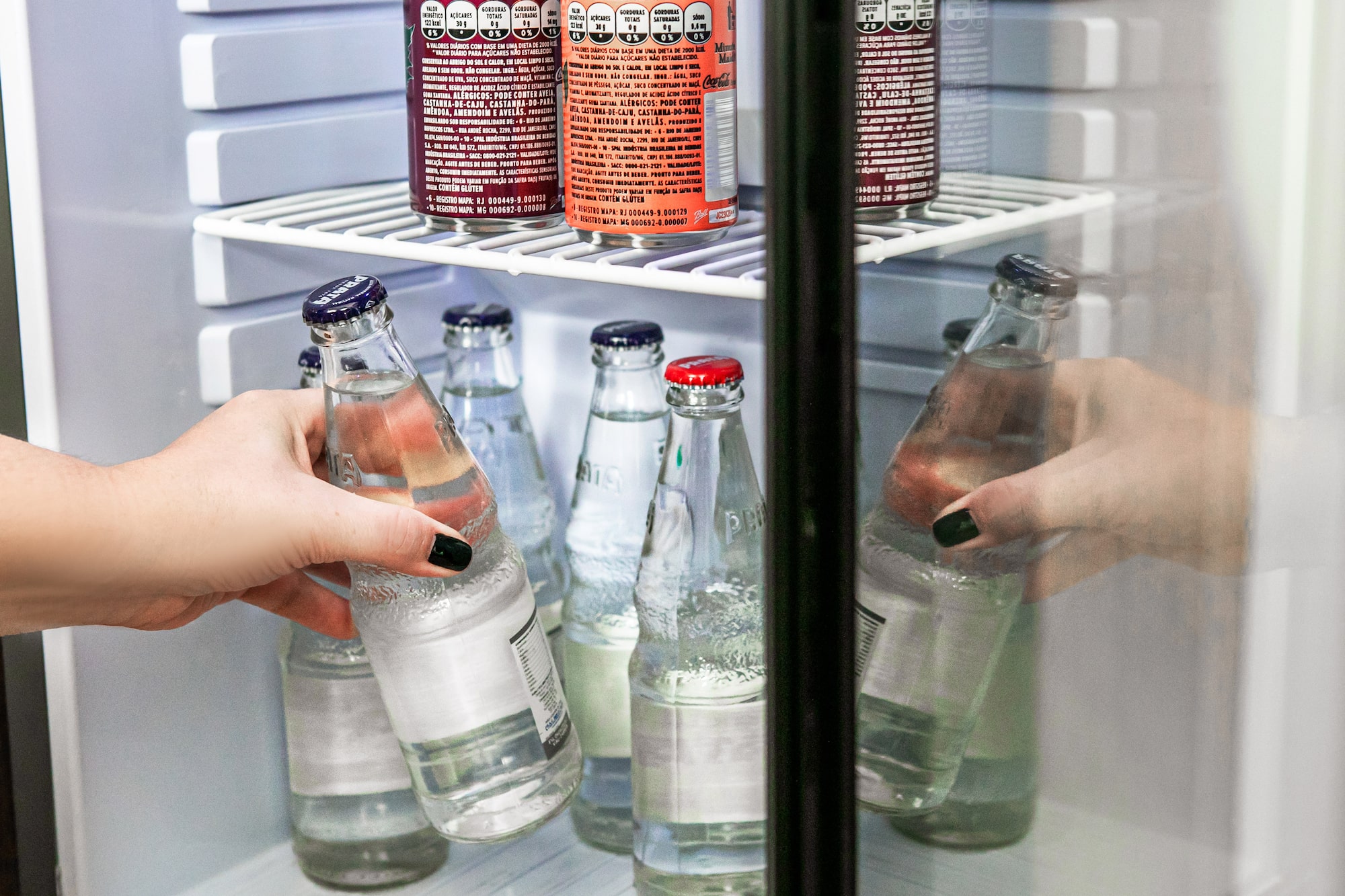 Hand grabbing bottled water from a hotel mini-bar refrigerator.