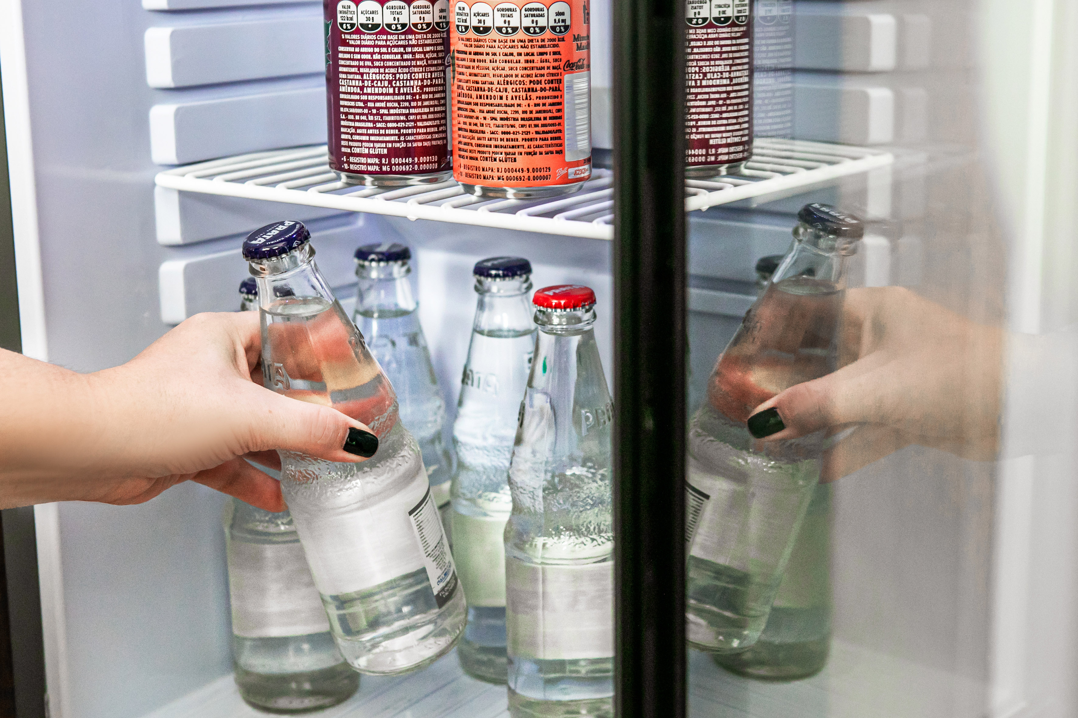 Hand grabbing bottled water from a hotel mini-bar refrigerator.