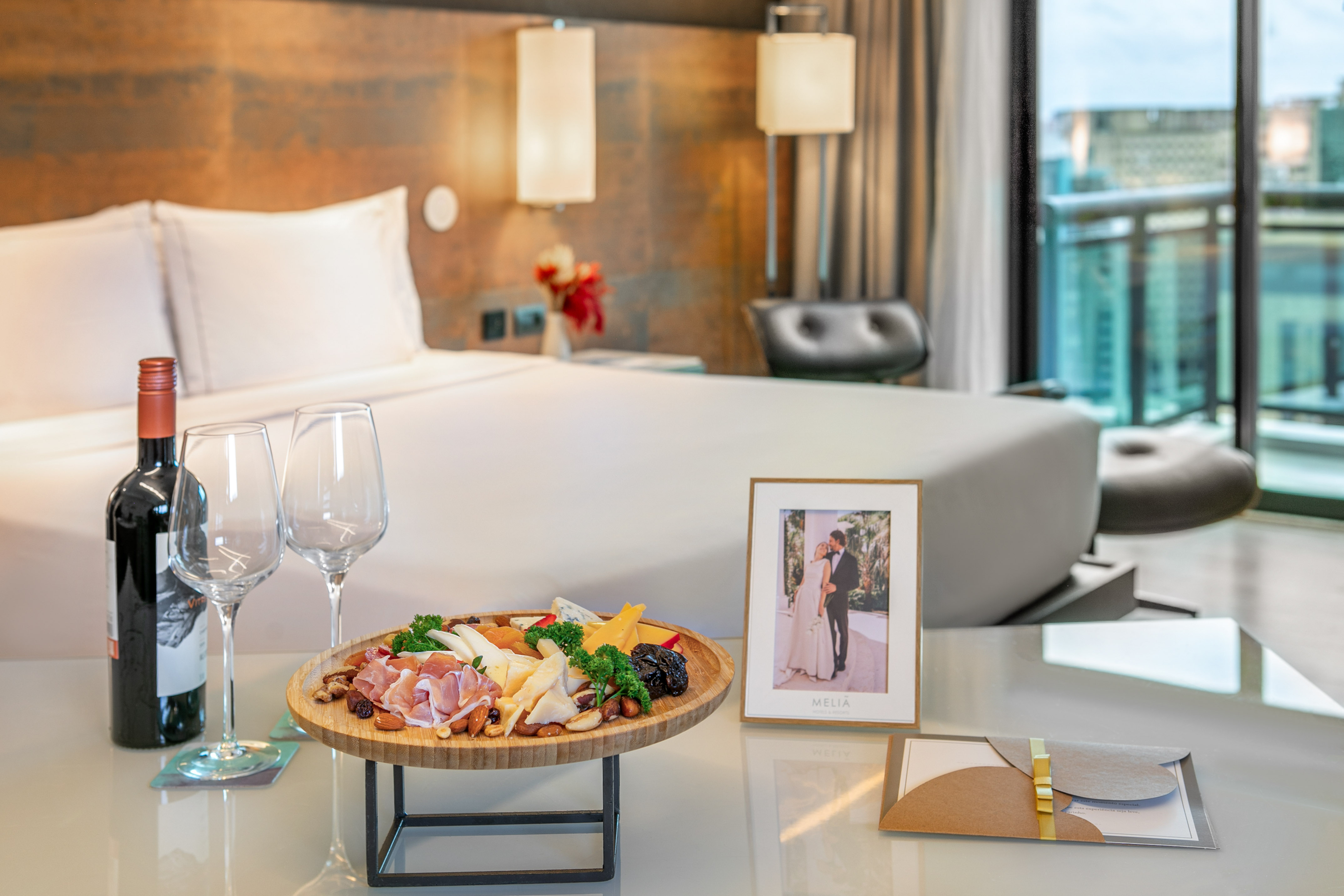 Romantic charcuterie board with wine, cheeses, cured meats, and fruits in a hotel room.