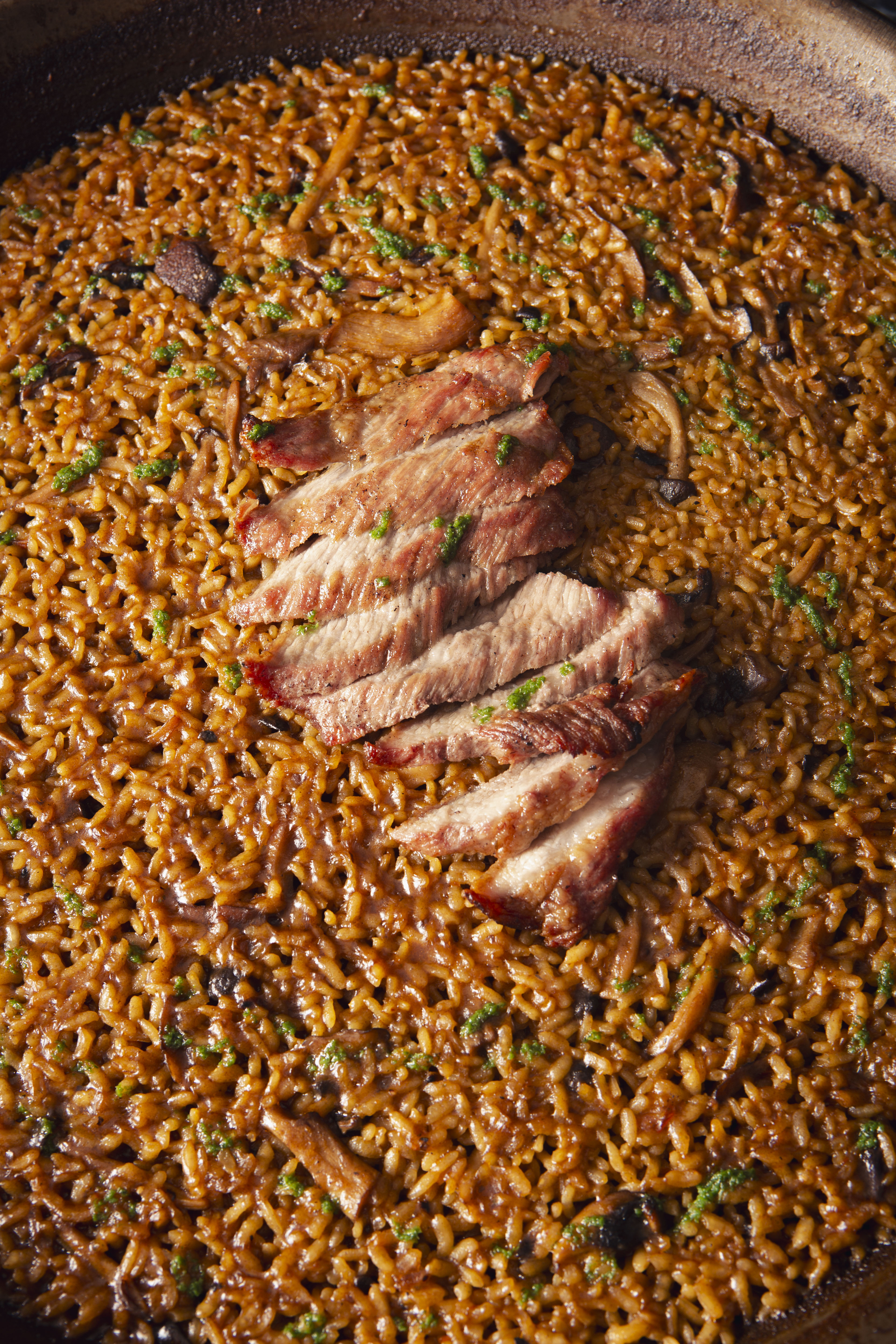 Arroz meloso with grilled pork slices, mushrooms, and parsley in a traditional paella pan.