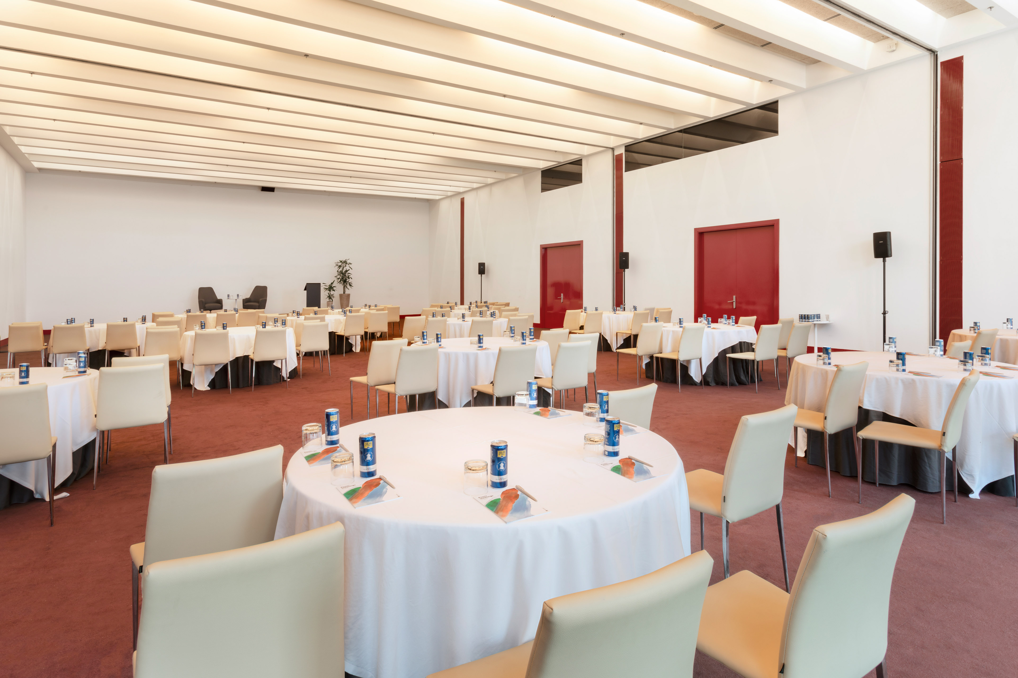 Empty conference room with round tables, beige chairs, and red carpet.