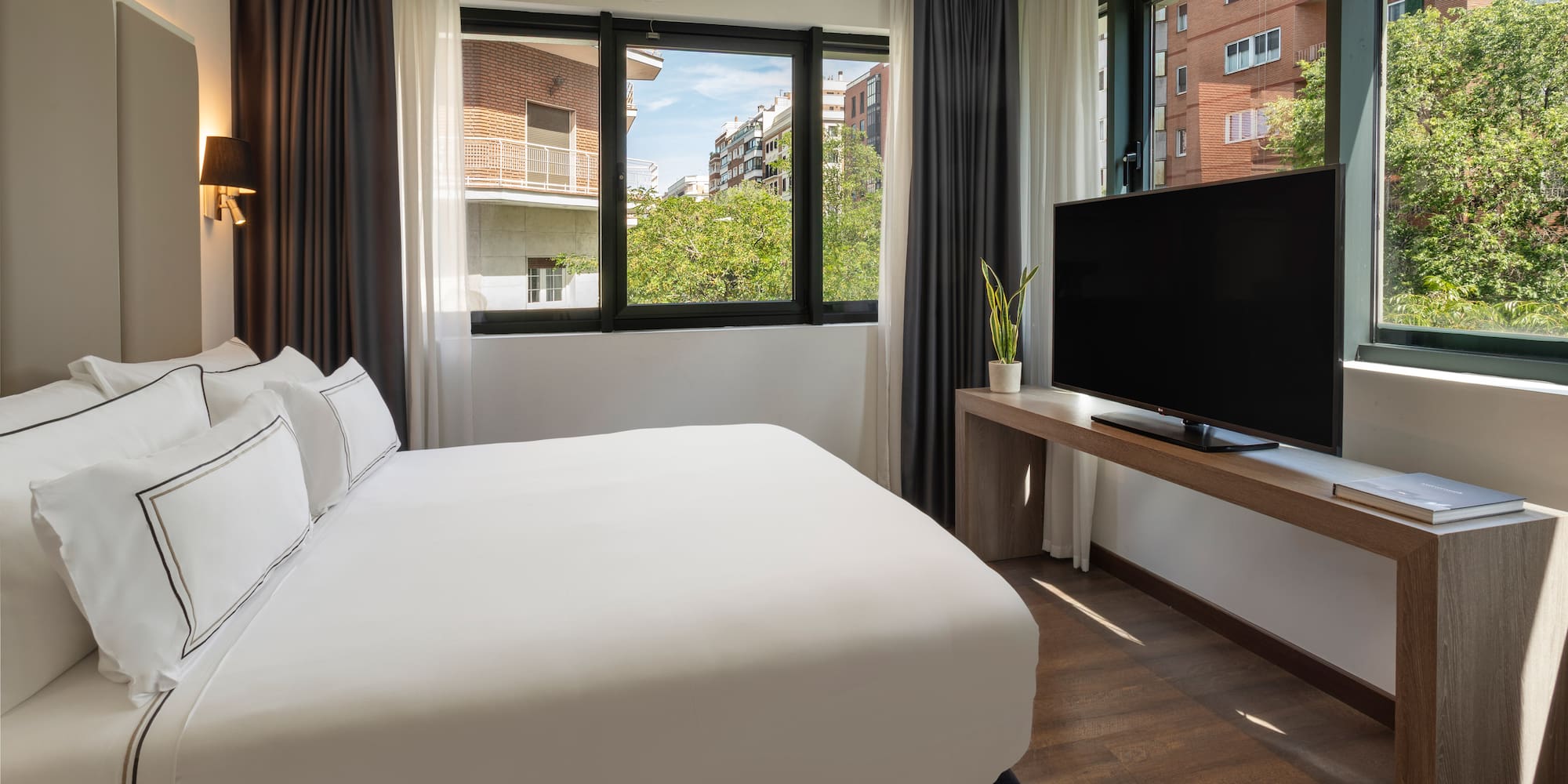 Habitación de hotel moderna con cama, TV y gran ventanal urbano.