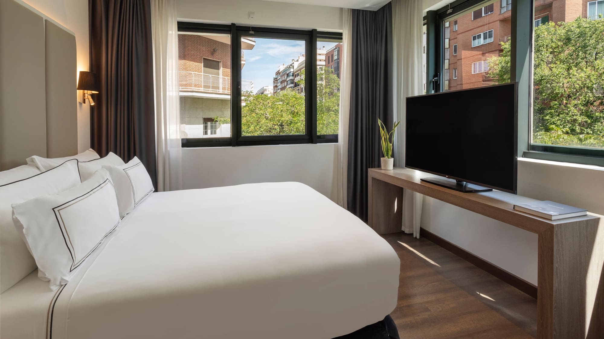 Habitación de hotel moderna con cama, TV y gran ventanal urbano.