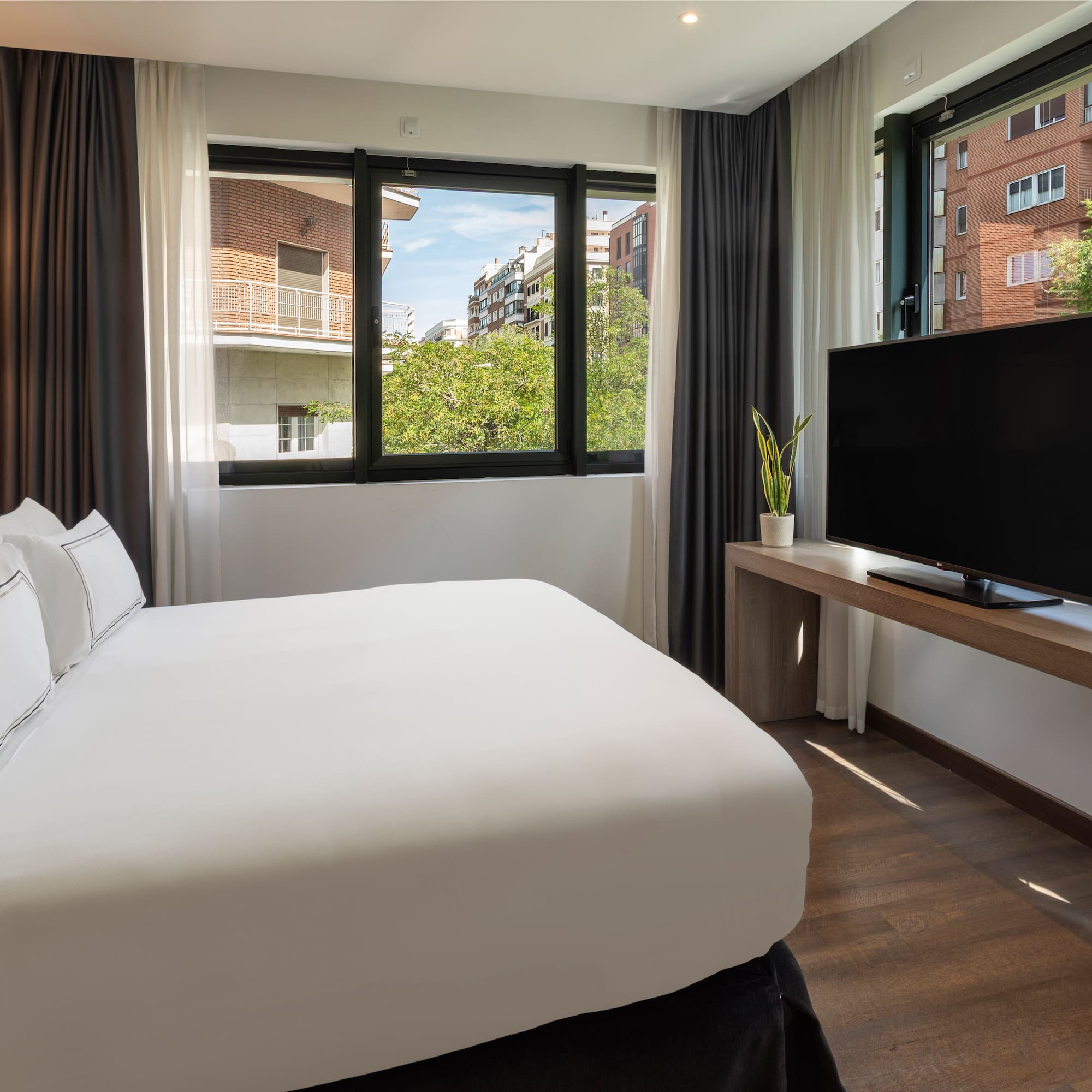 Habitación de hotel moderna con cama, TV y gran ventanal urbano.