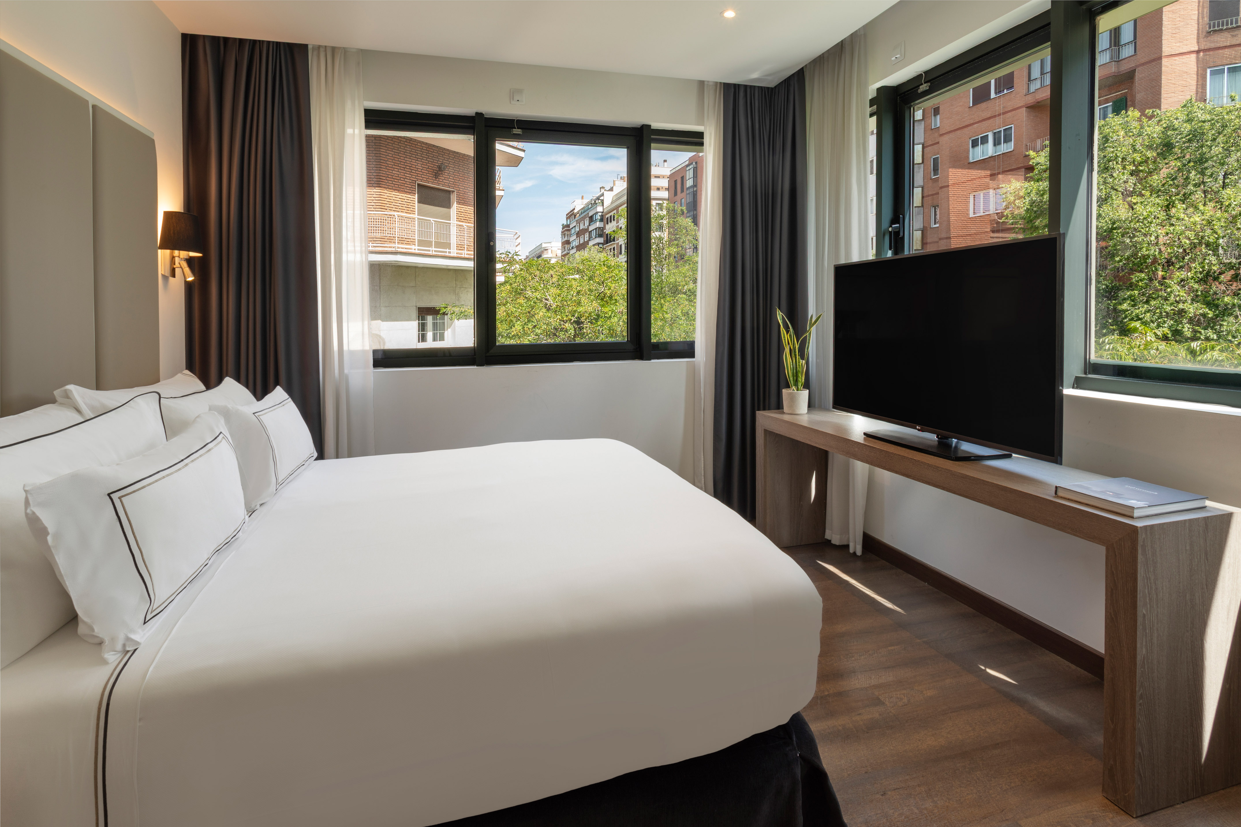 Habitación de hotel moderna con cama, TV y gran ventanal urbano.