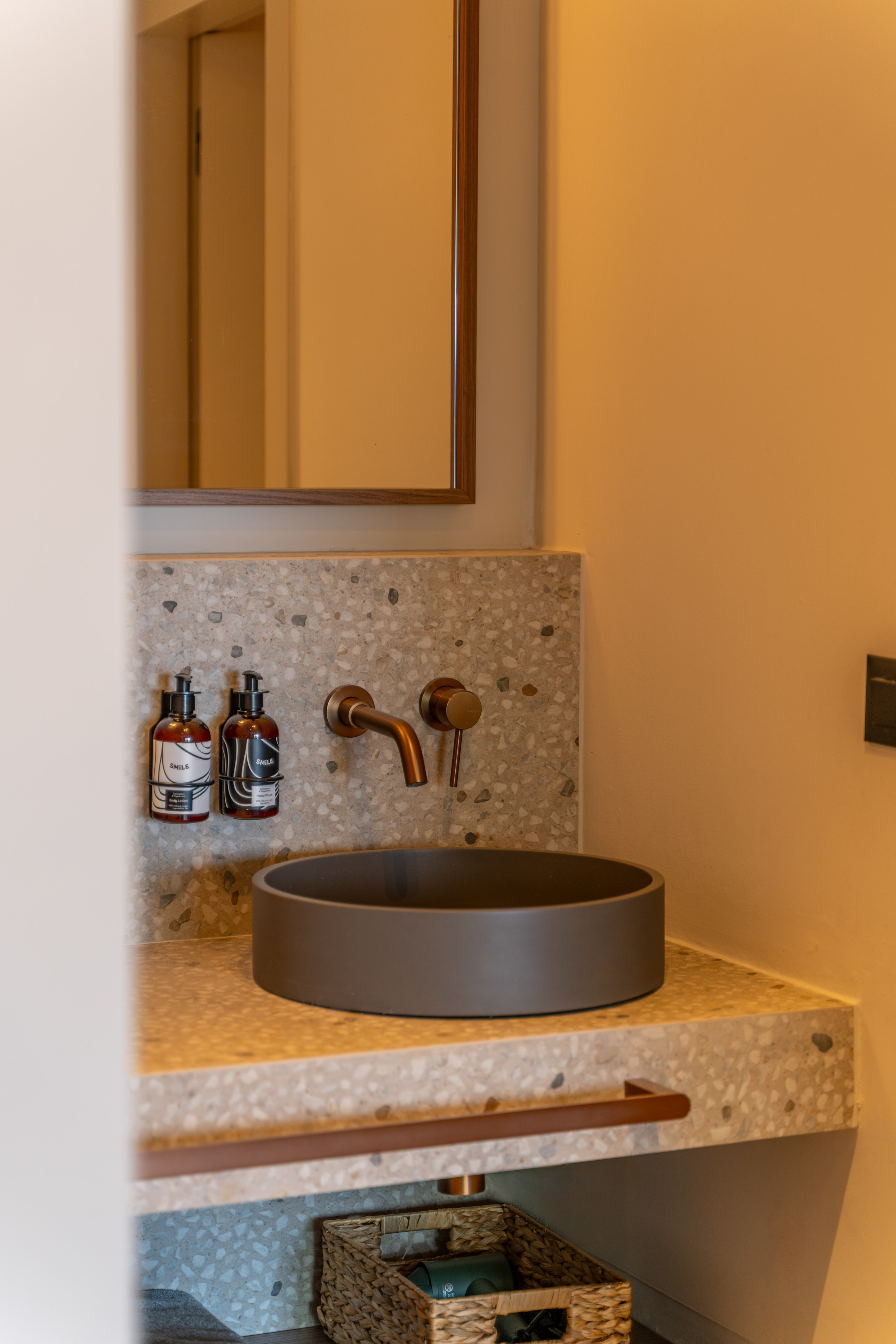 Modern bathroom vanity with dark basin, bronze faucet, terrazzo counter.