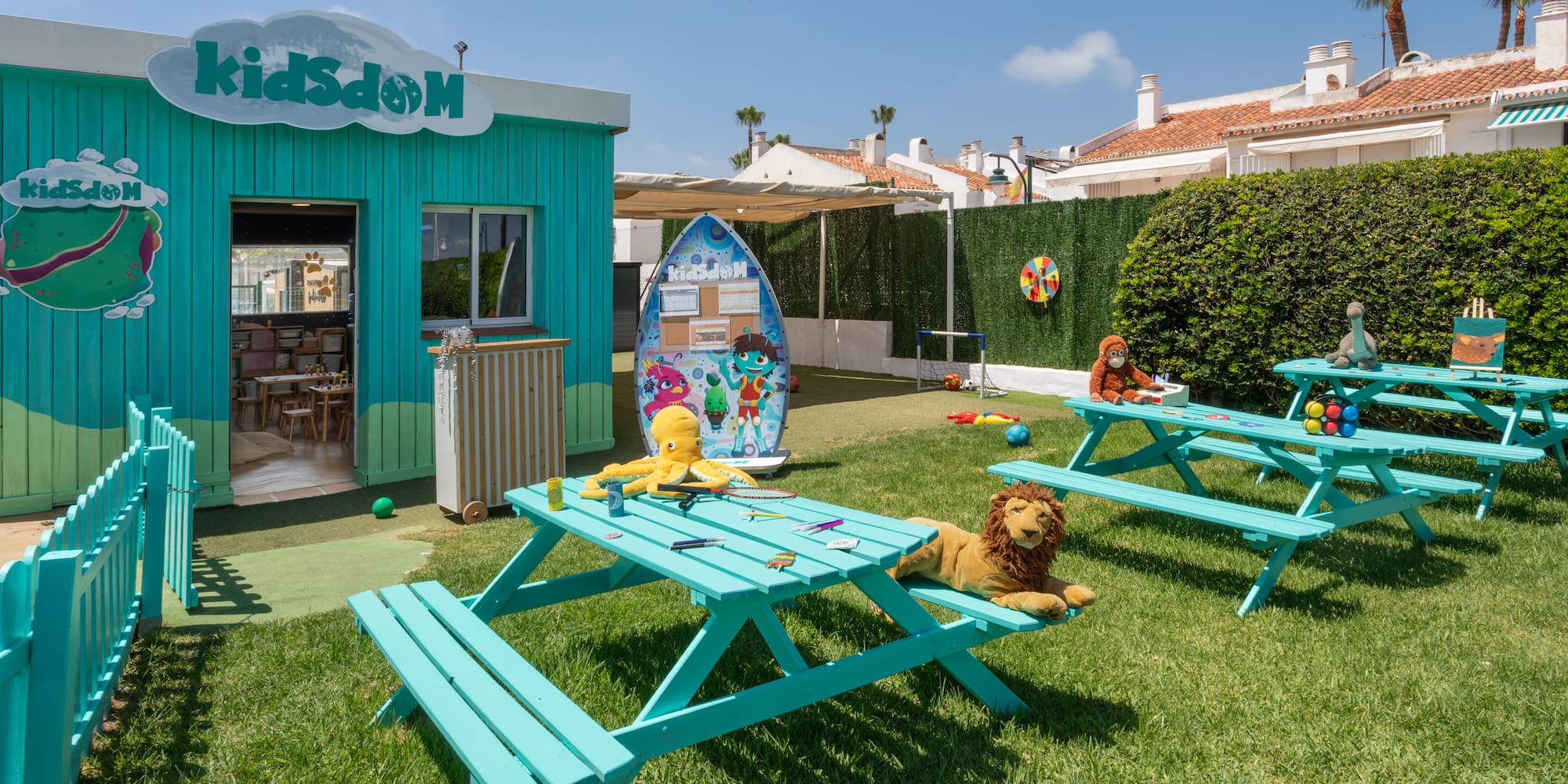Resort kids club outdoor play area with turquoise tables and toys on grass.