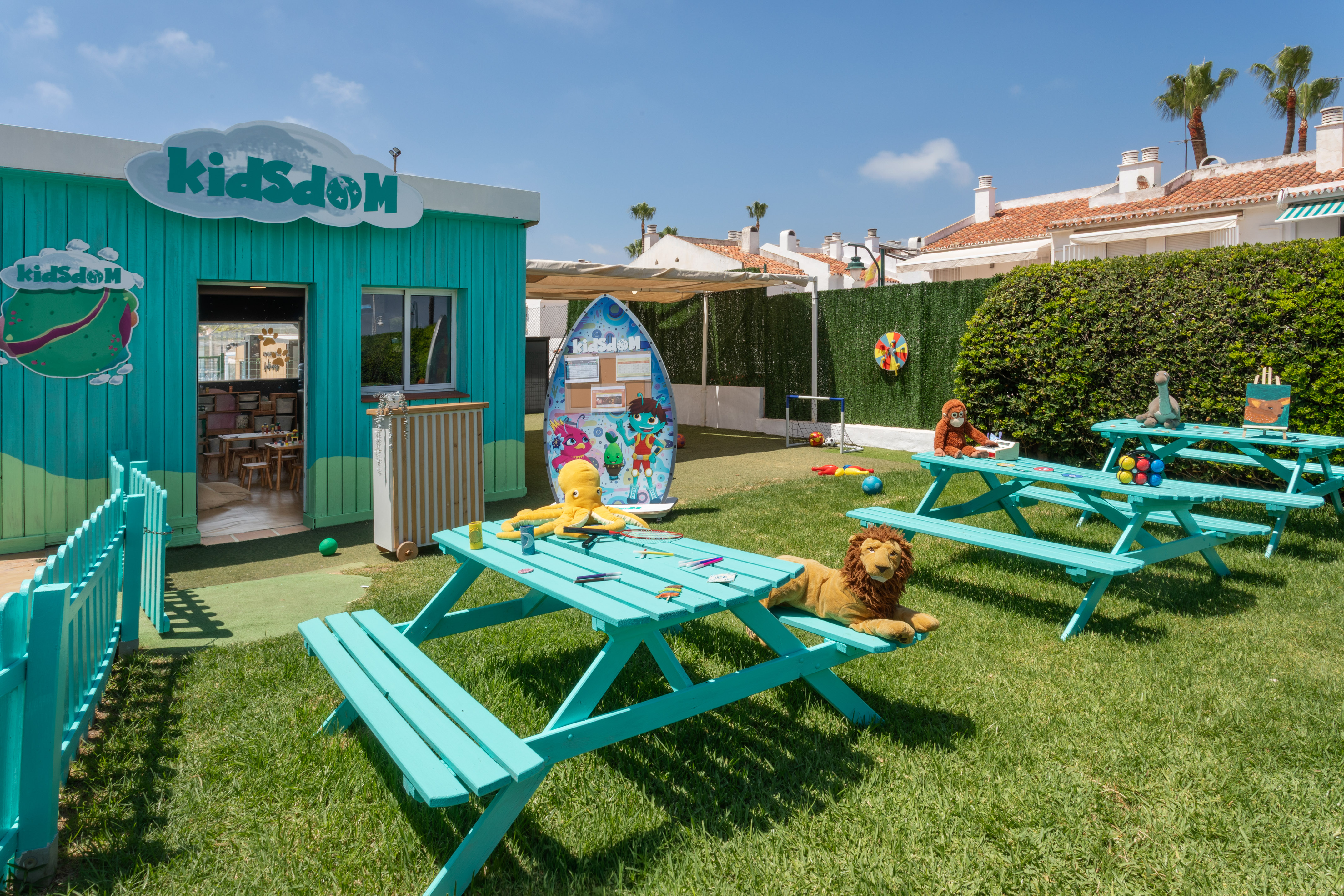Resort kids club outdoor play area with turquoise tables and toys on grass.
