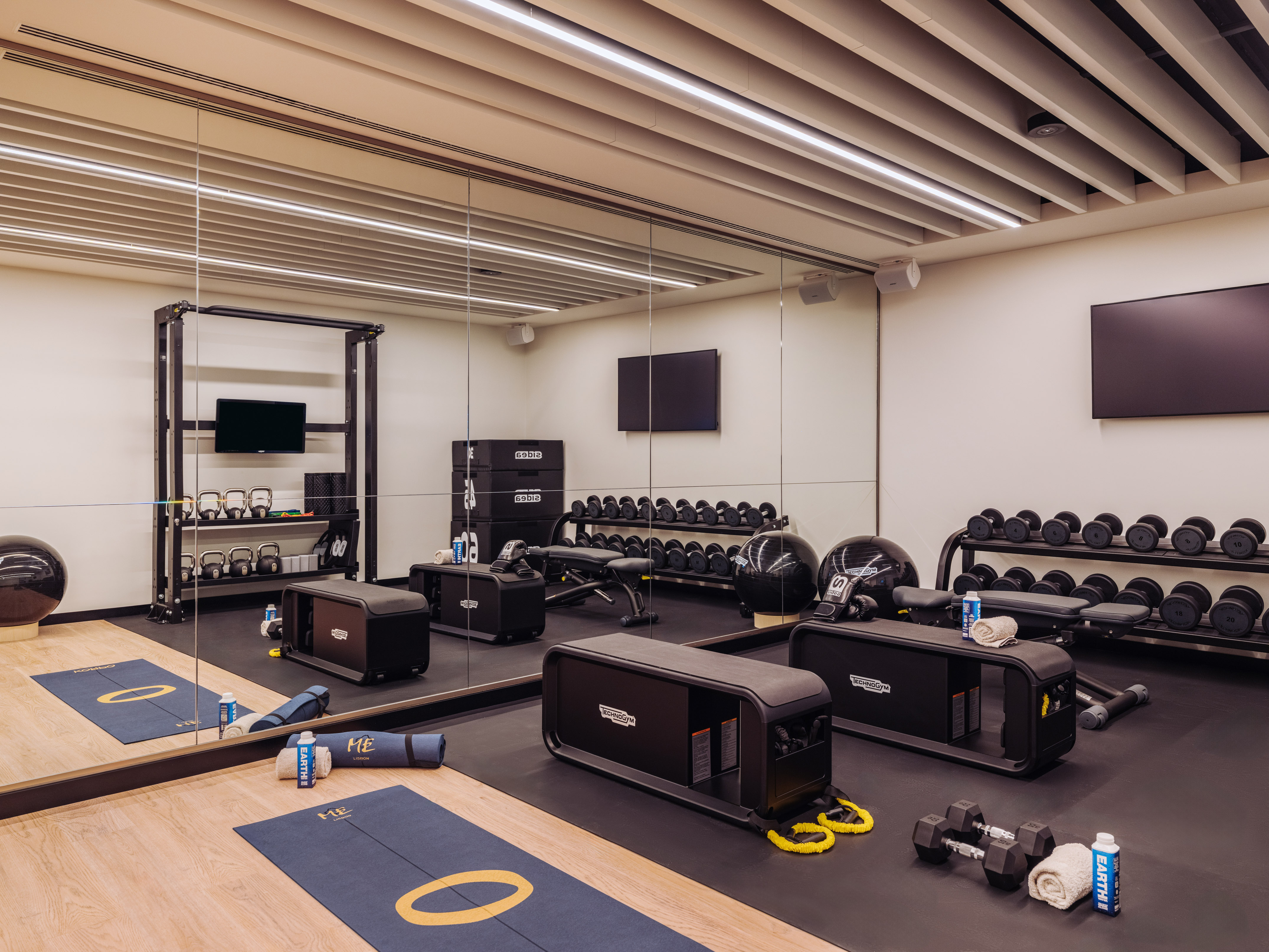Sleek gym with Technogym equipment, dumbbells, kettlebells, and workout mats.