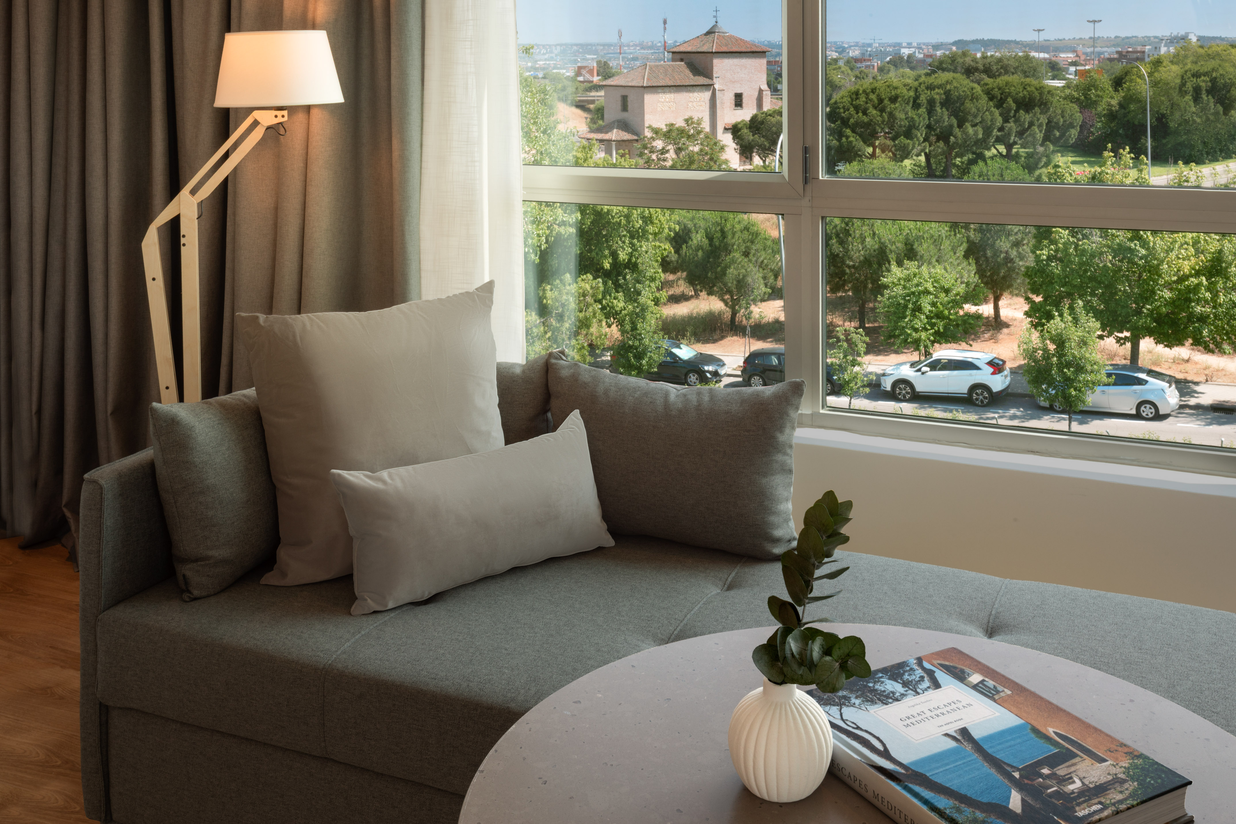 Grey sofa, modern lamp, and city view from a hotel room window.