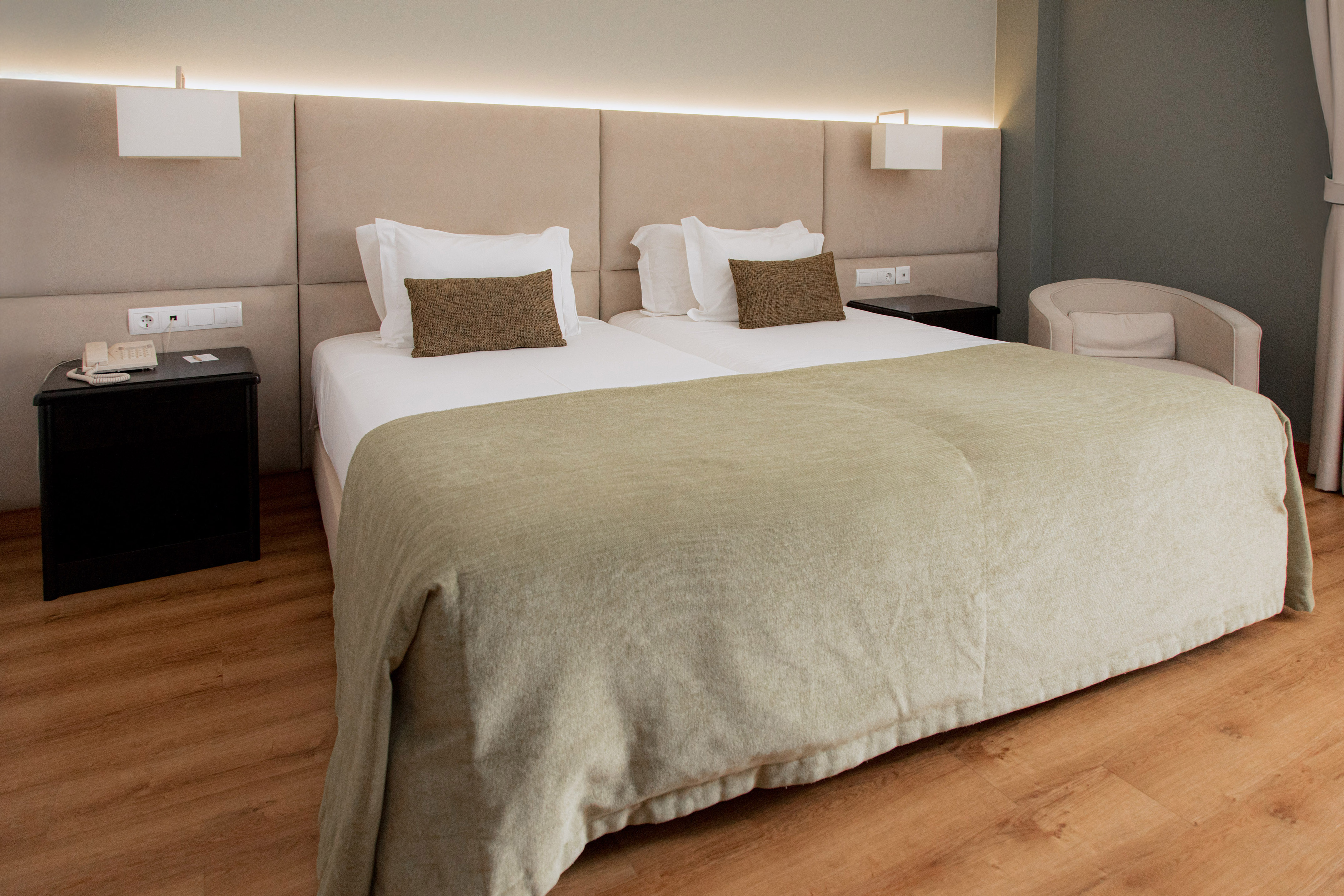 Modern hotel room with twin beds, padded headboard, and wooden floor.