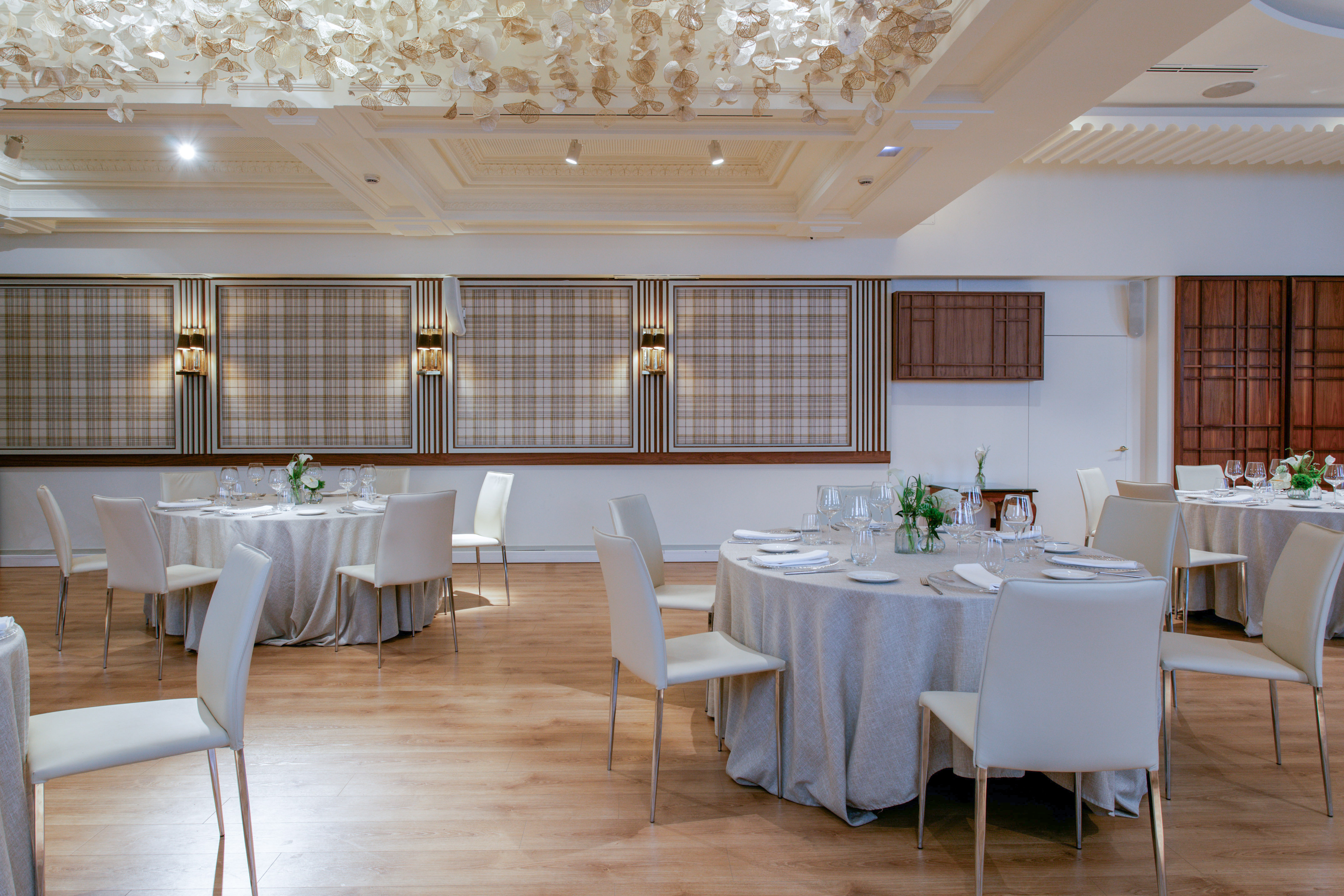 Elegant banquet room with set round tables, white chairs, and decorative ceiling.
