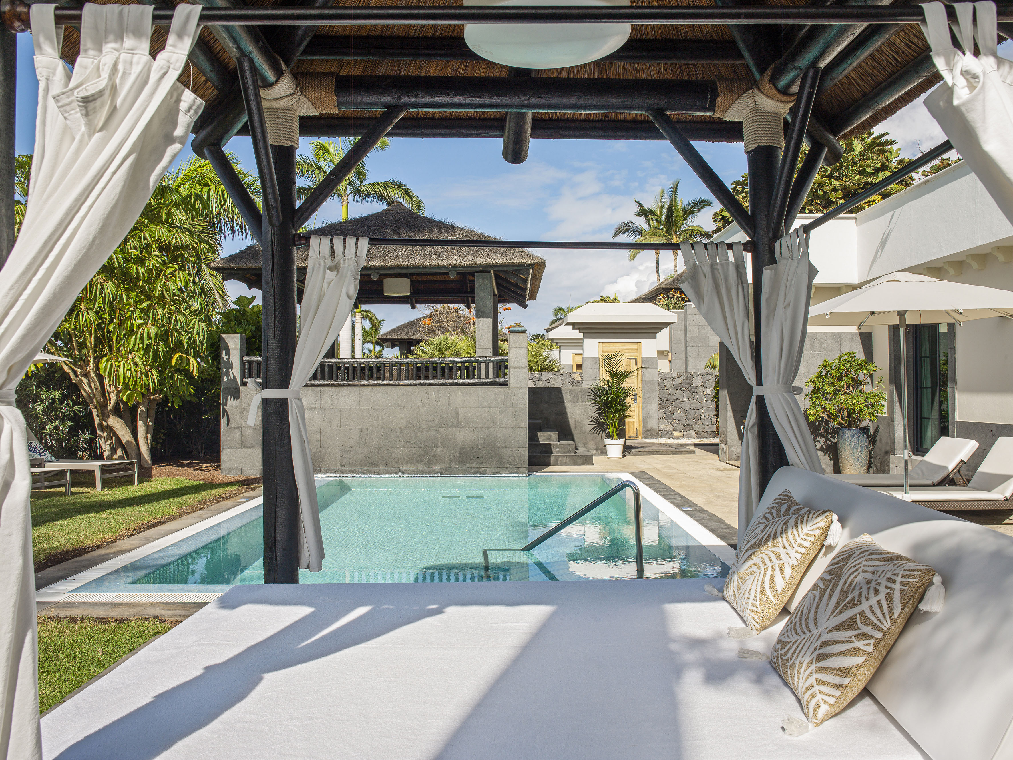 Luxury tropical resort pool view from a shaded canopy daybed.