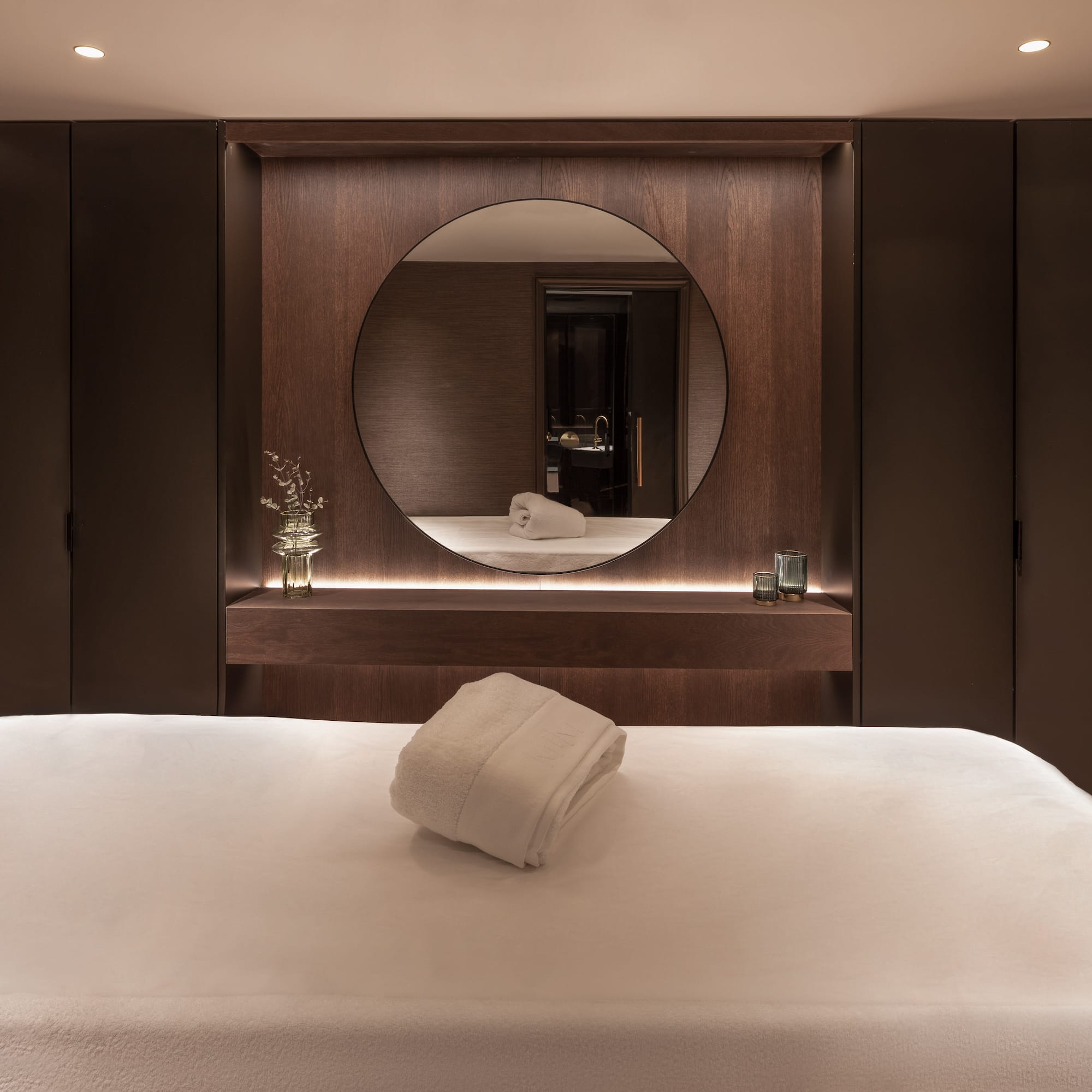 Luxury spa treatment room with dark wood walls, round mirror, and massage table.