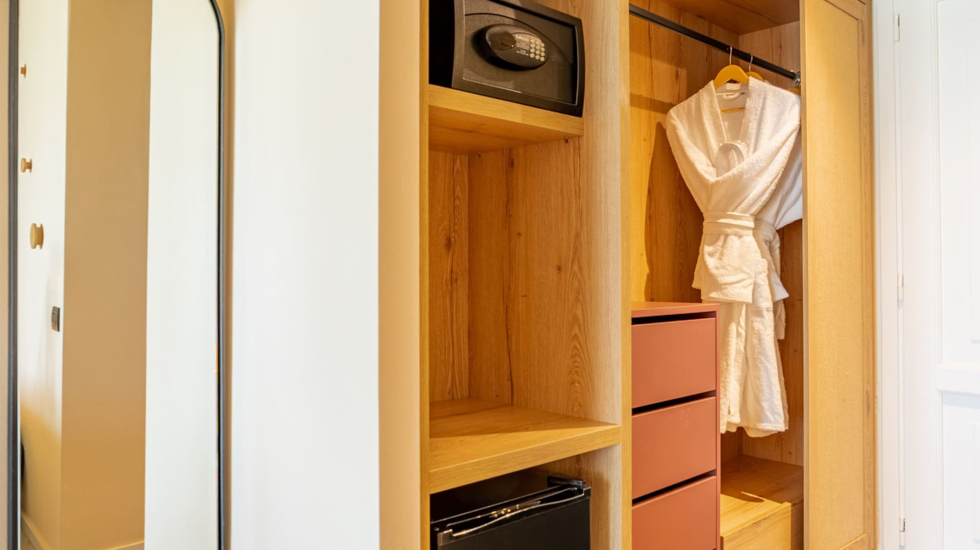 Hotel room modern wooden closet with safe, mini-fridge, and mirror.