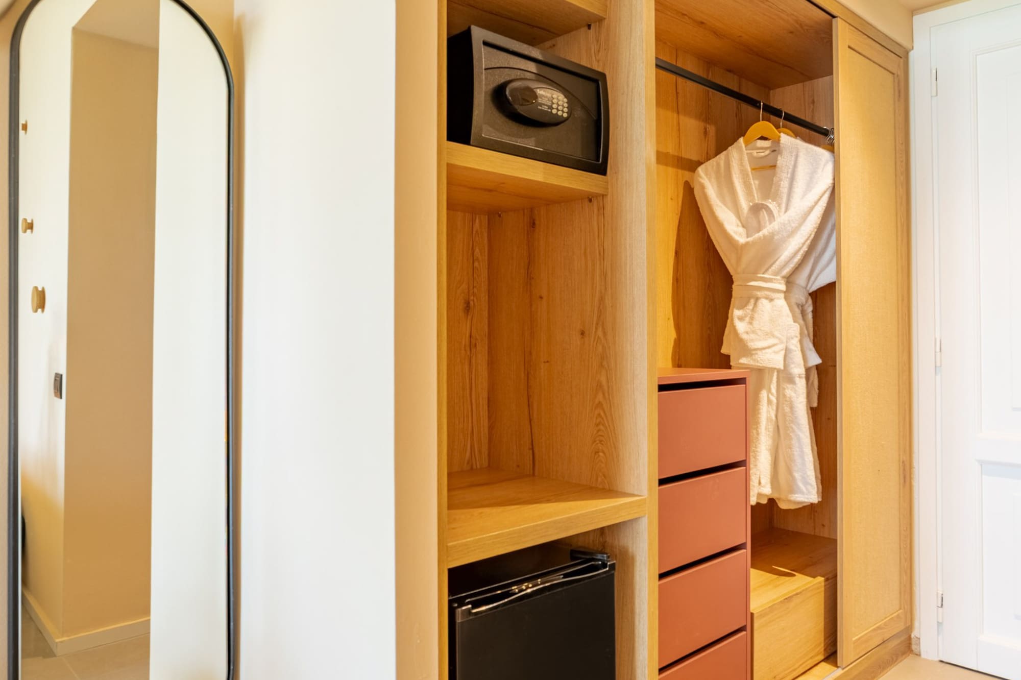 Hotel room modern wooden closet with safe, mini-fridge, and mirror.