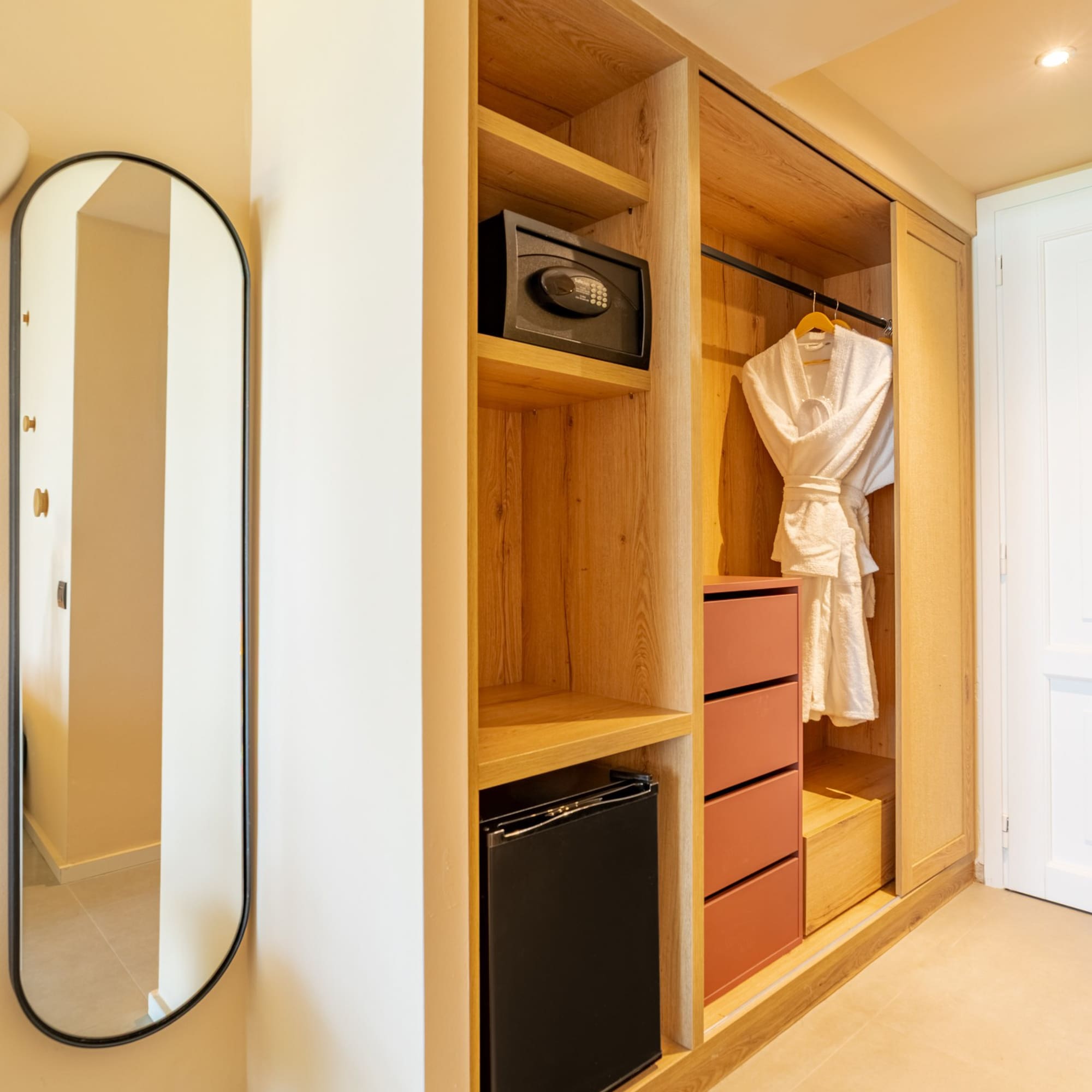 Hotel room modern wooden closet with safe, mini-fridge, and mirror.