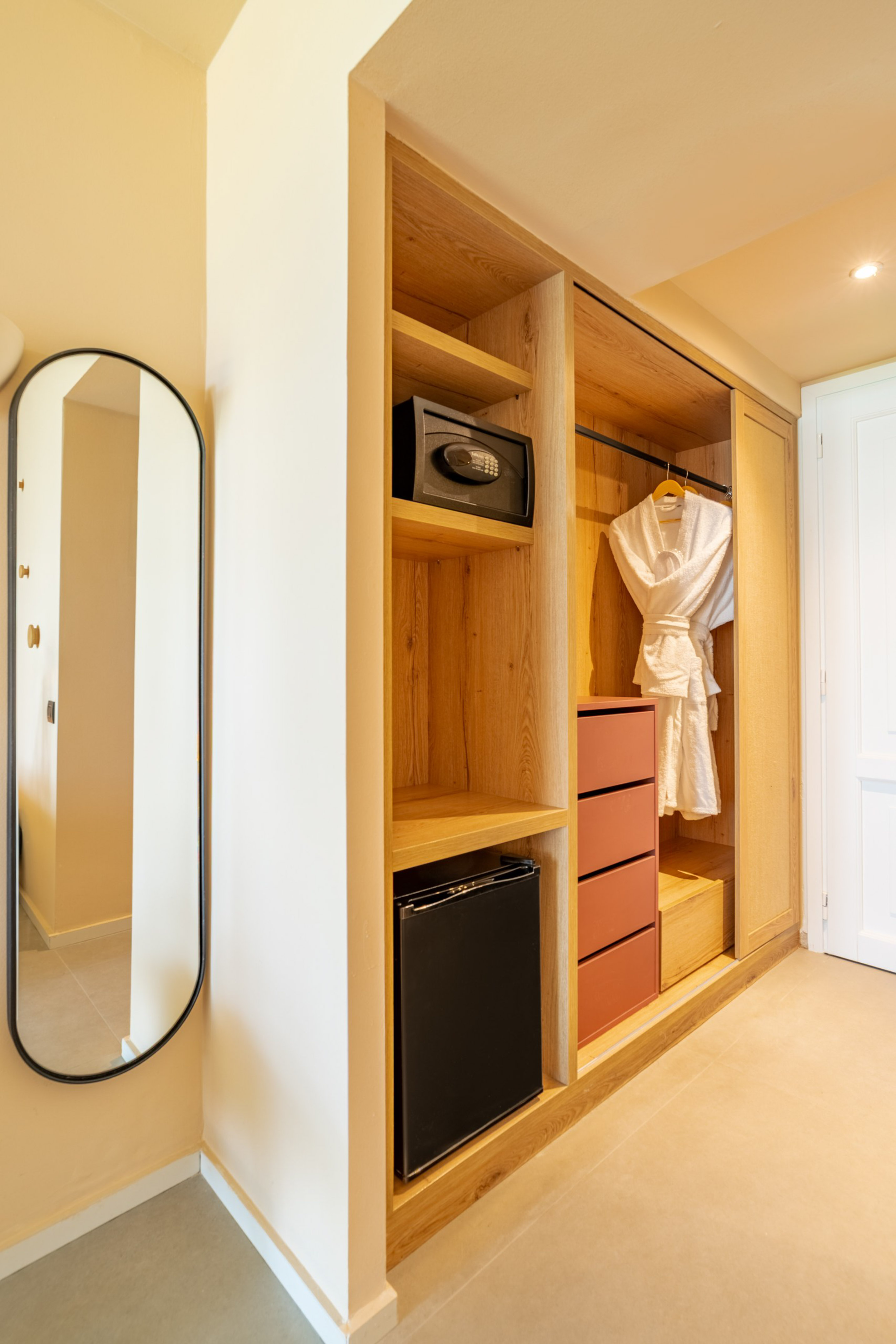 Hotel room modern wooden closet with safe, mini-fridge, and mirror.