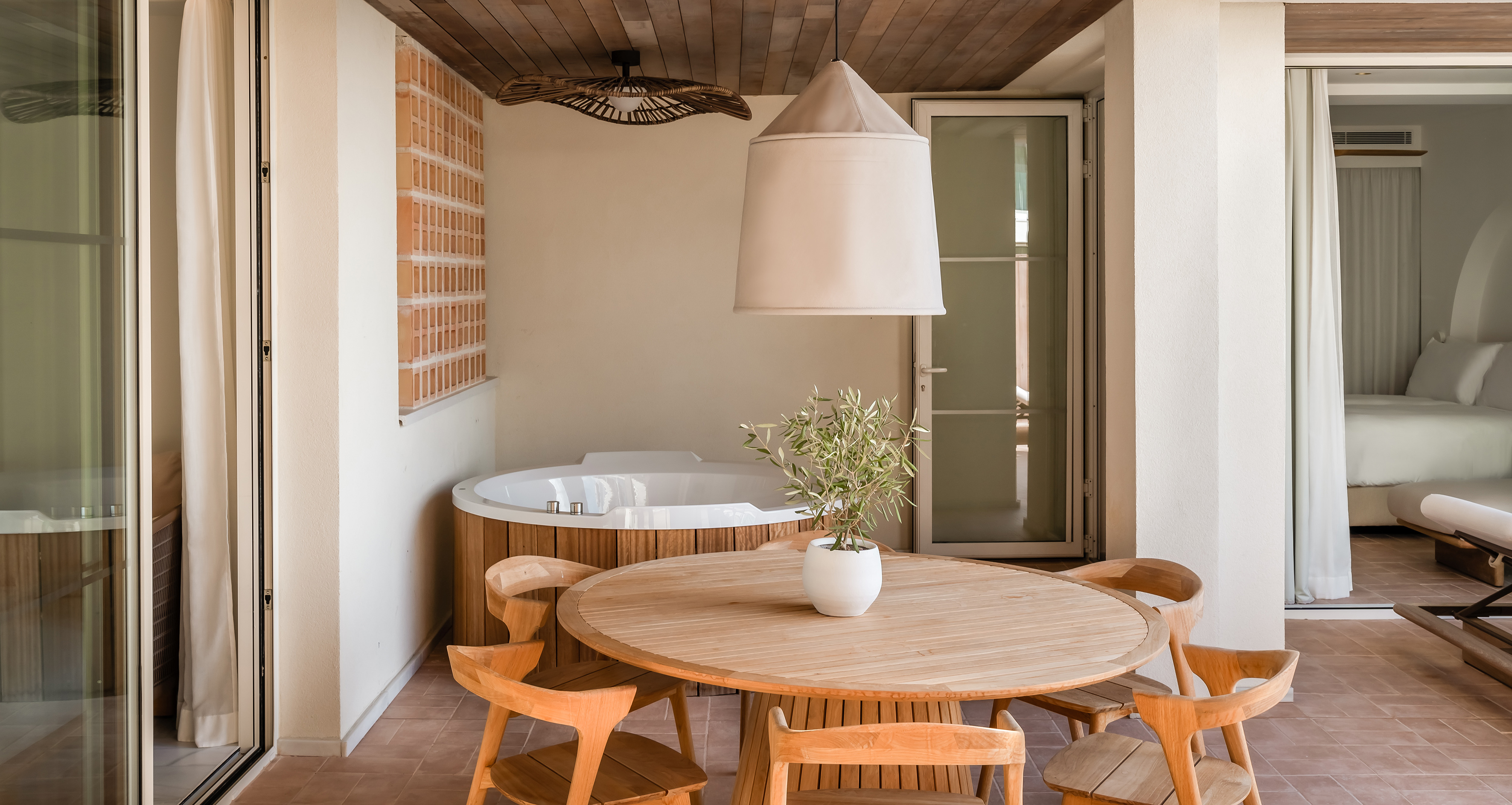 Patio with private hot tub, wooden dining set, and adjoining modern bedroom.