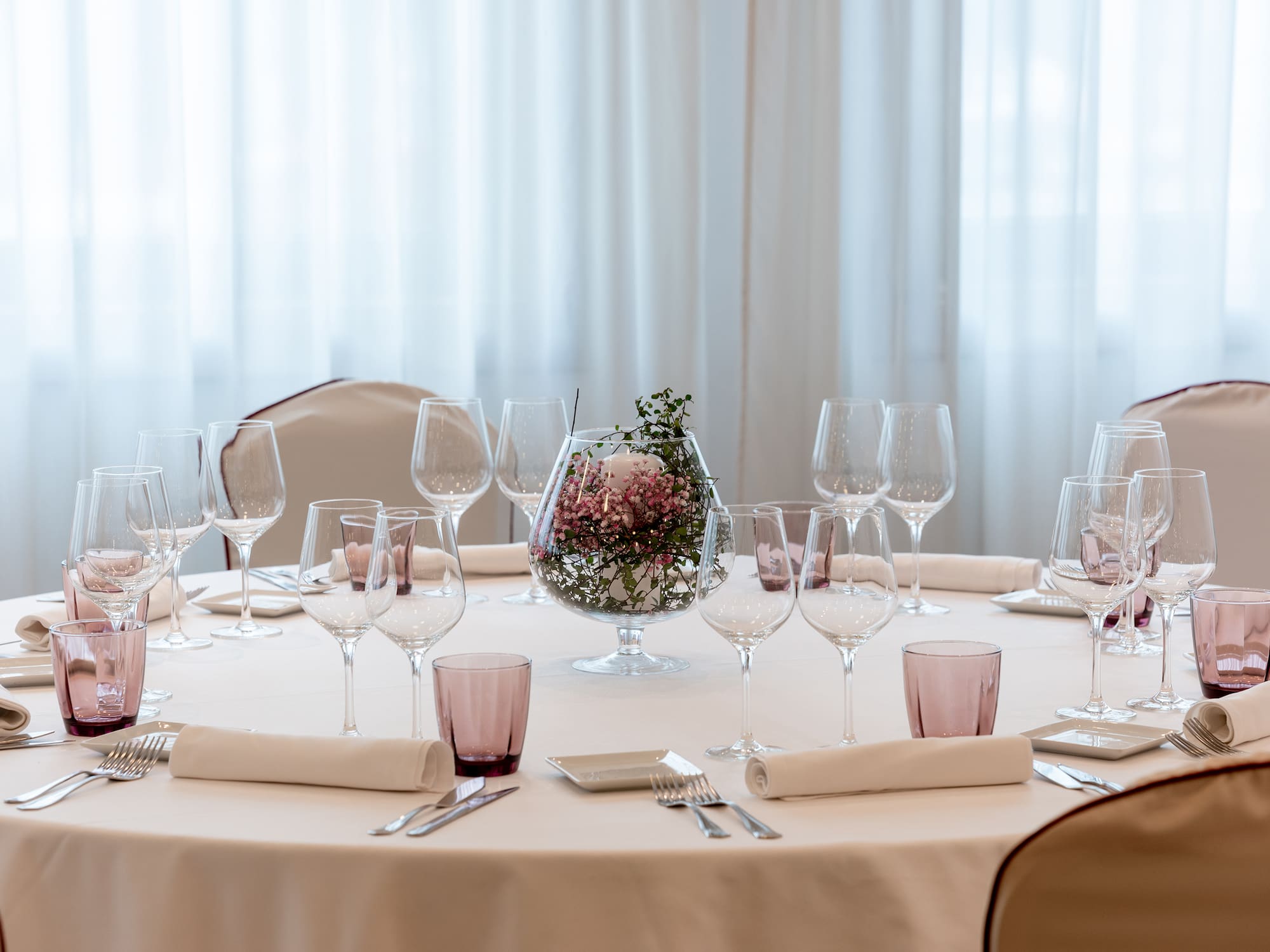Elegant round table set with pink floral centerpiece, wine glasses, white linens.