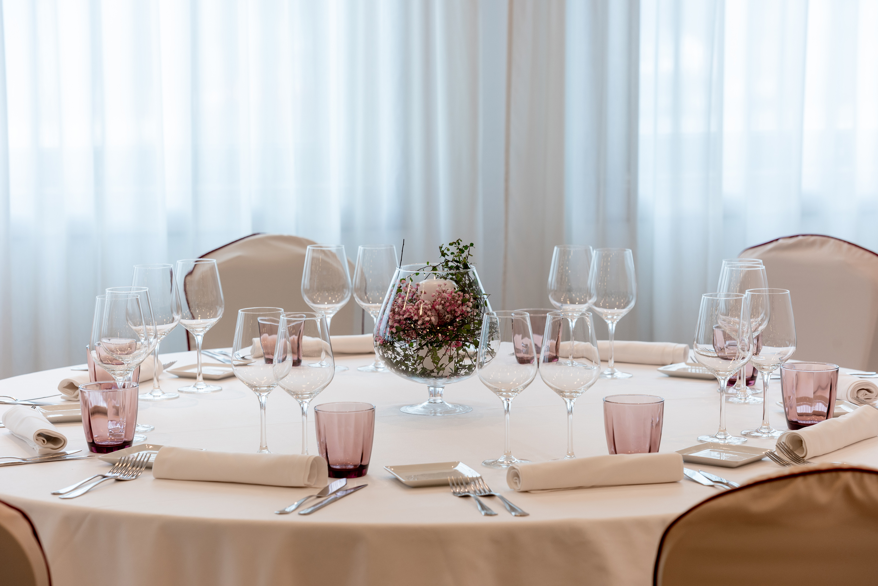 Elegant round table set with pink floral centerpiece, wine glasses, white linens.